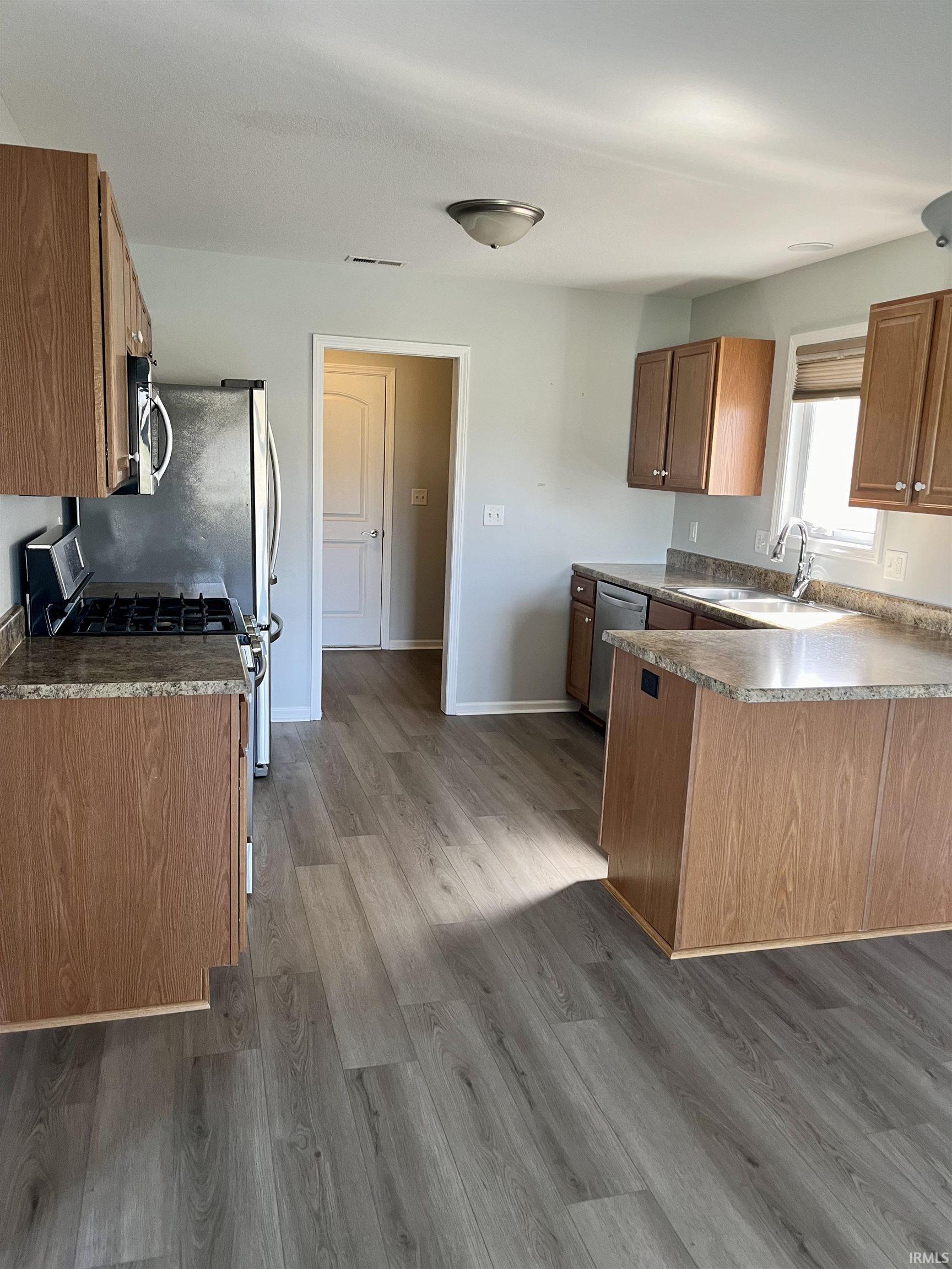 Kitchen with a peninsula, wood finish cabinets, stainless steel appliances, and dark wood-style floors