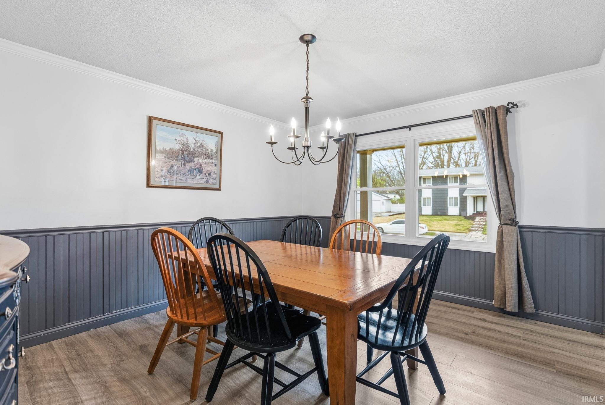 Dining room featuring wainscoting, a chandelier, ornamental molding, and light wood-style floors