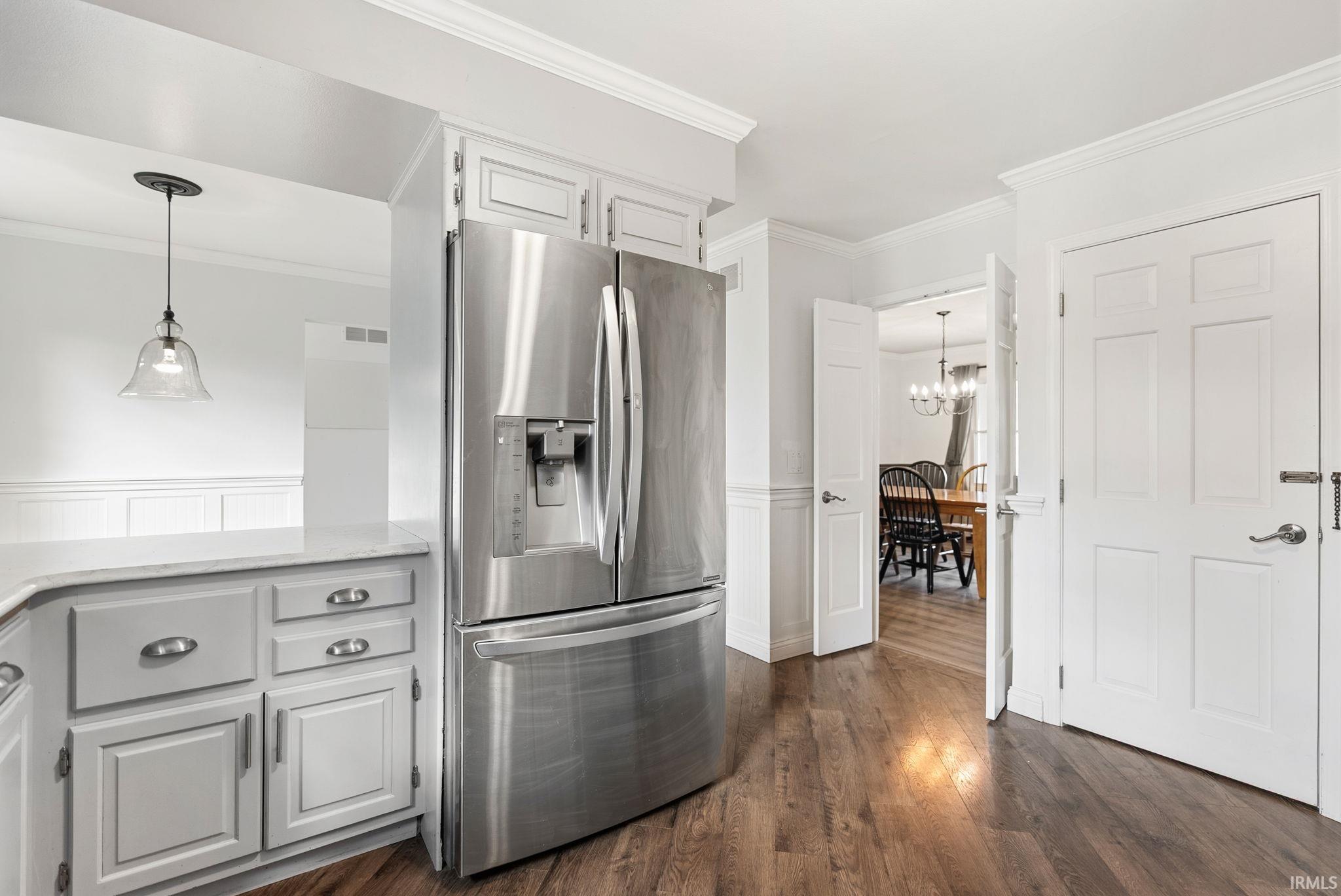 Kitchen featuring stainless steel refrigerator with ice dispenser, crown molding, a wainscoted wall, white cabinetry, and dark wood-style flooring