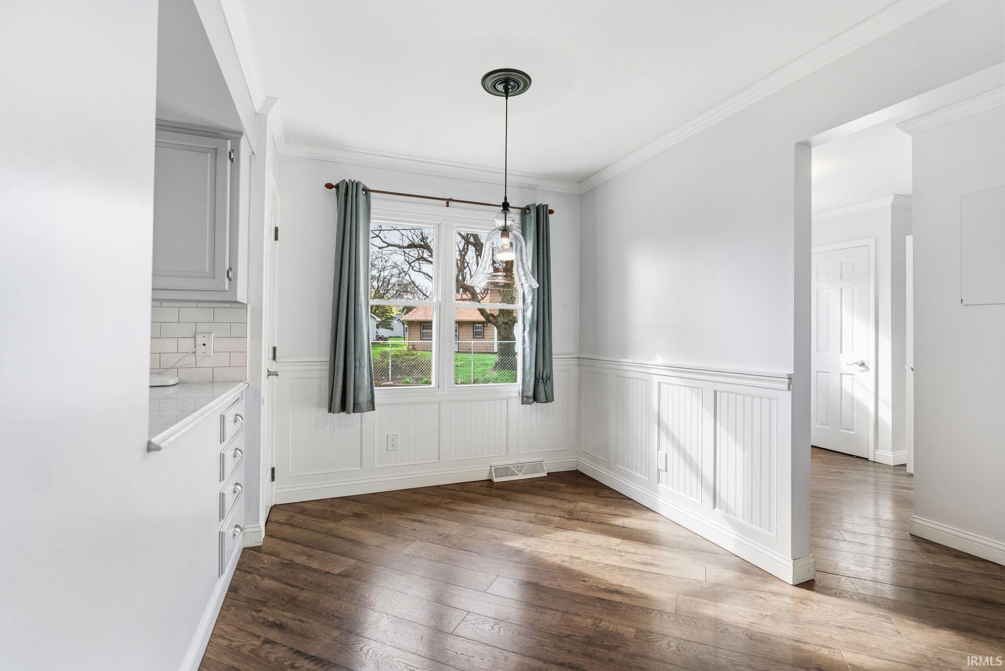 Unfurnished dining area with ornamental molding, dark wood-style floors, and wainscoting