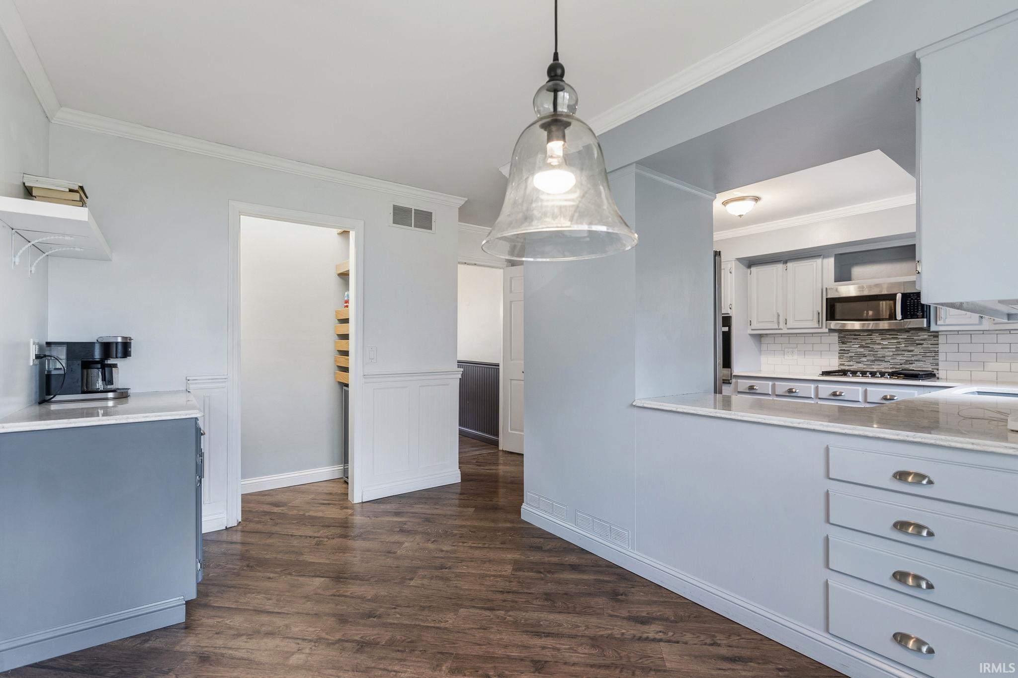 Kitchen featuring light stone countertops, ornamental molding, dark wood-style floors, white cabinets, and hanging light fixtures
