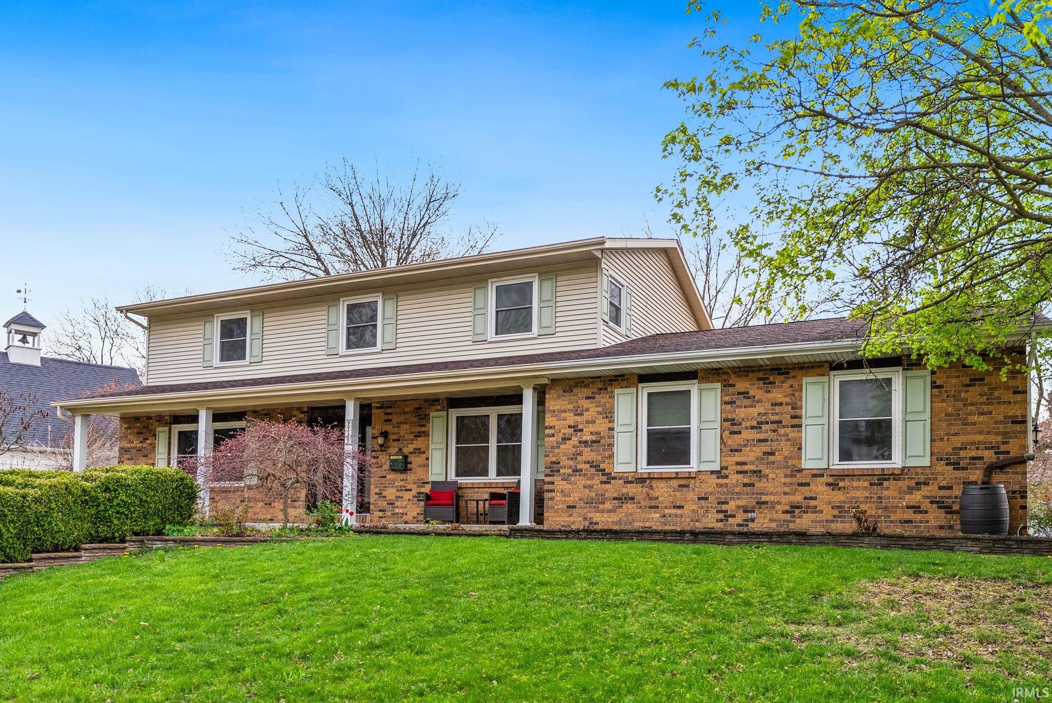 Traditional home featuring brick siding, a front yard, and a porch