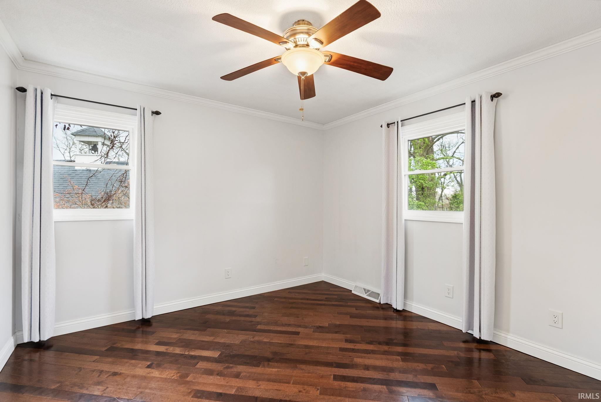 Spare room with dark wood-style floors, crown molding, and a ceiling fan