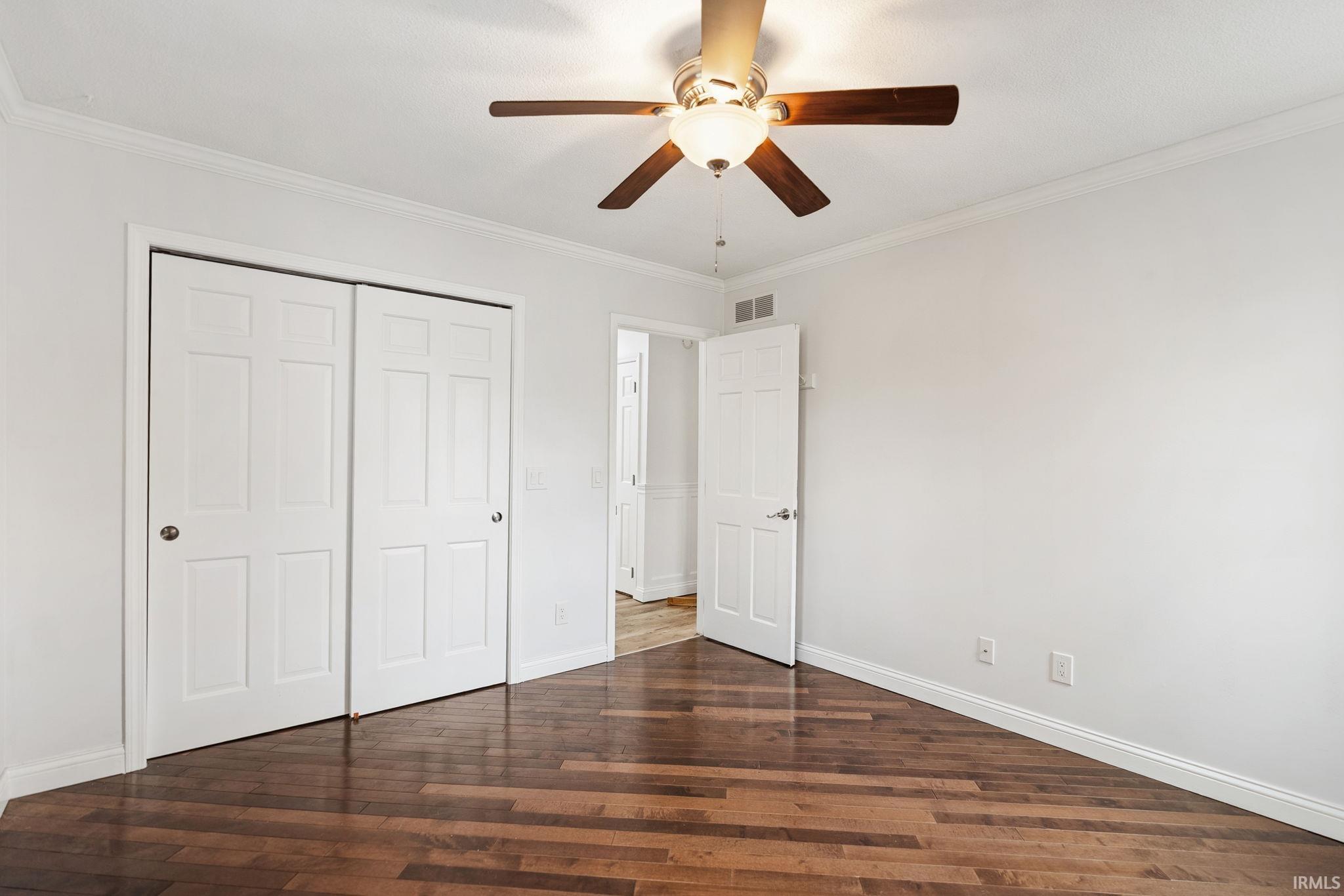 Unfurnished bedroom with dark wood finished floors, ornamental molding, a ceiling fan, and a closet