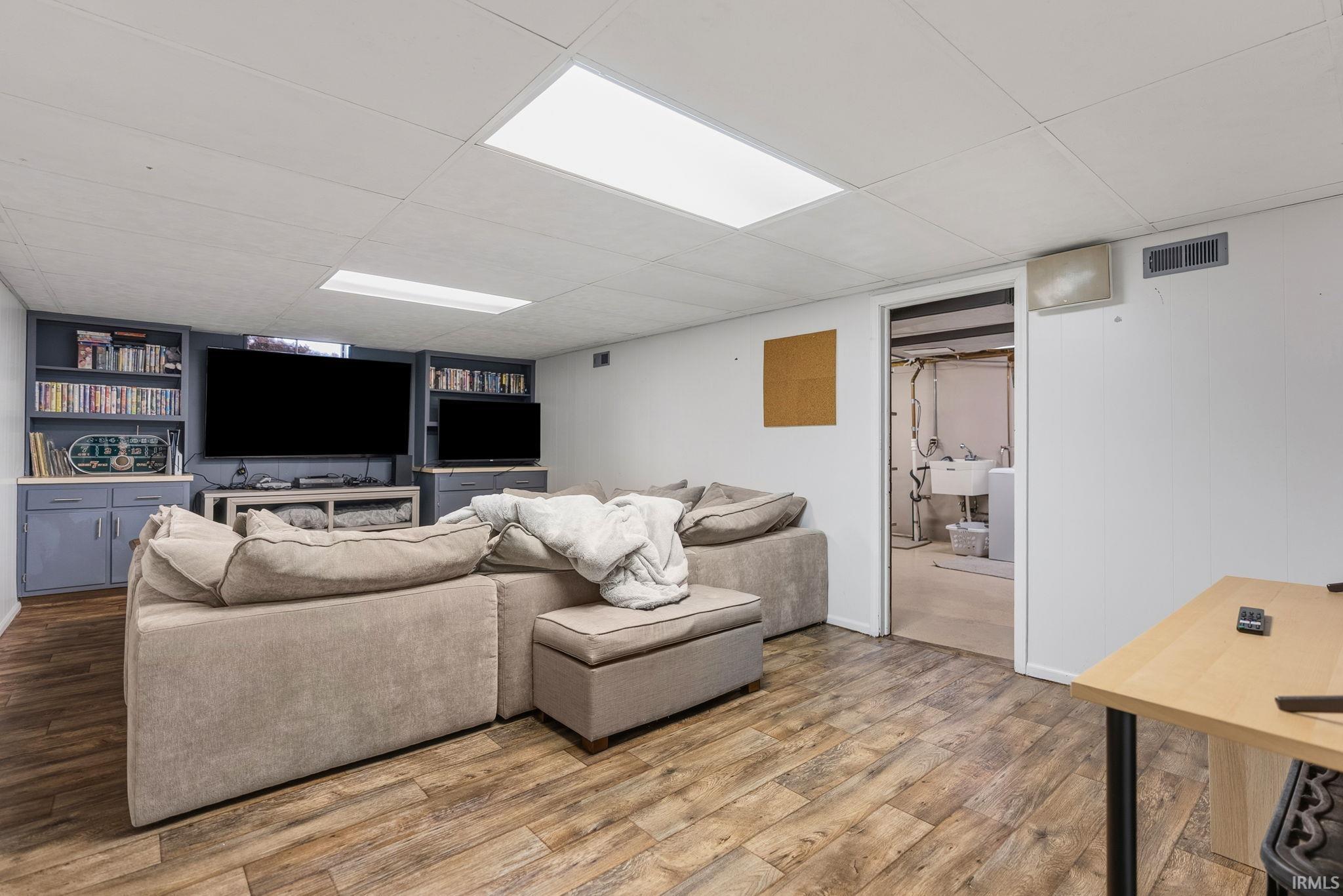 Living room featuring a paneled ceiling, light wood-type flooring, and built in shelves