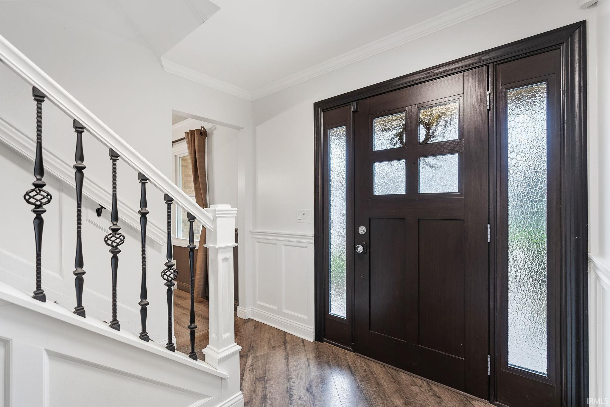 Foyer entrance with dark wood-style flooring, crown molding, healthy amount of natural light, a wainscoted wall, and a decorative wall