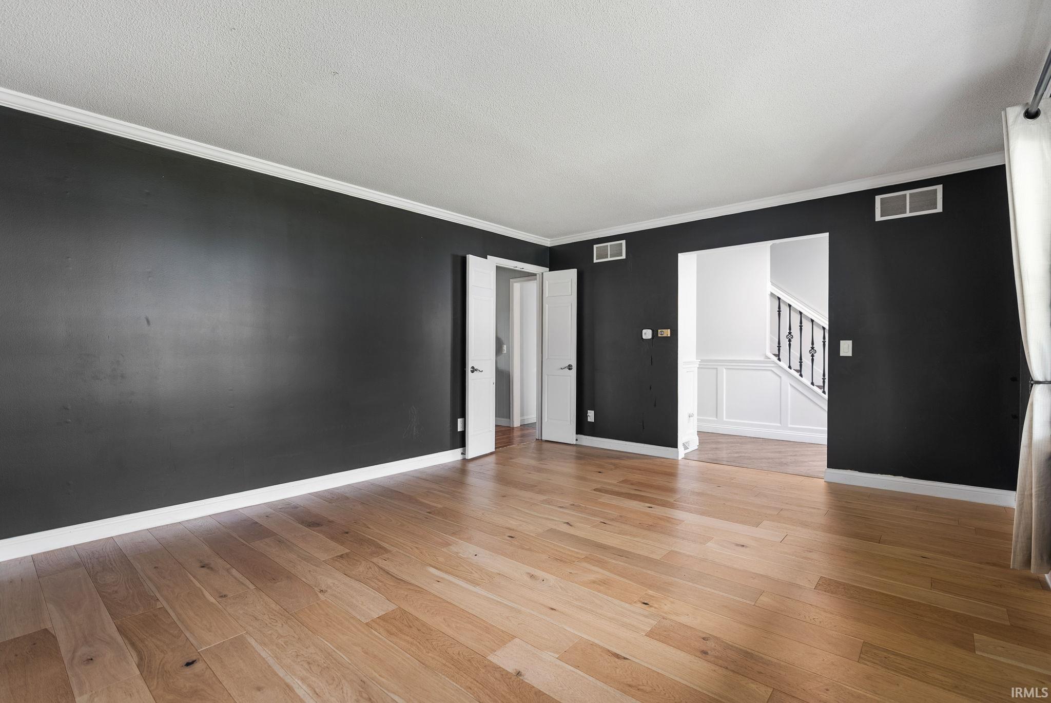 Unfurnished room featuring ornamental molding, light wood-style floors, and a textured ceiling