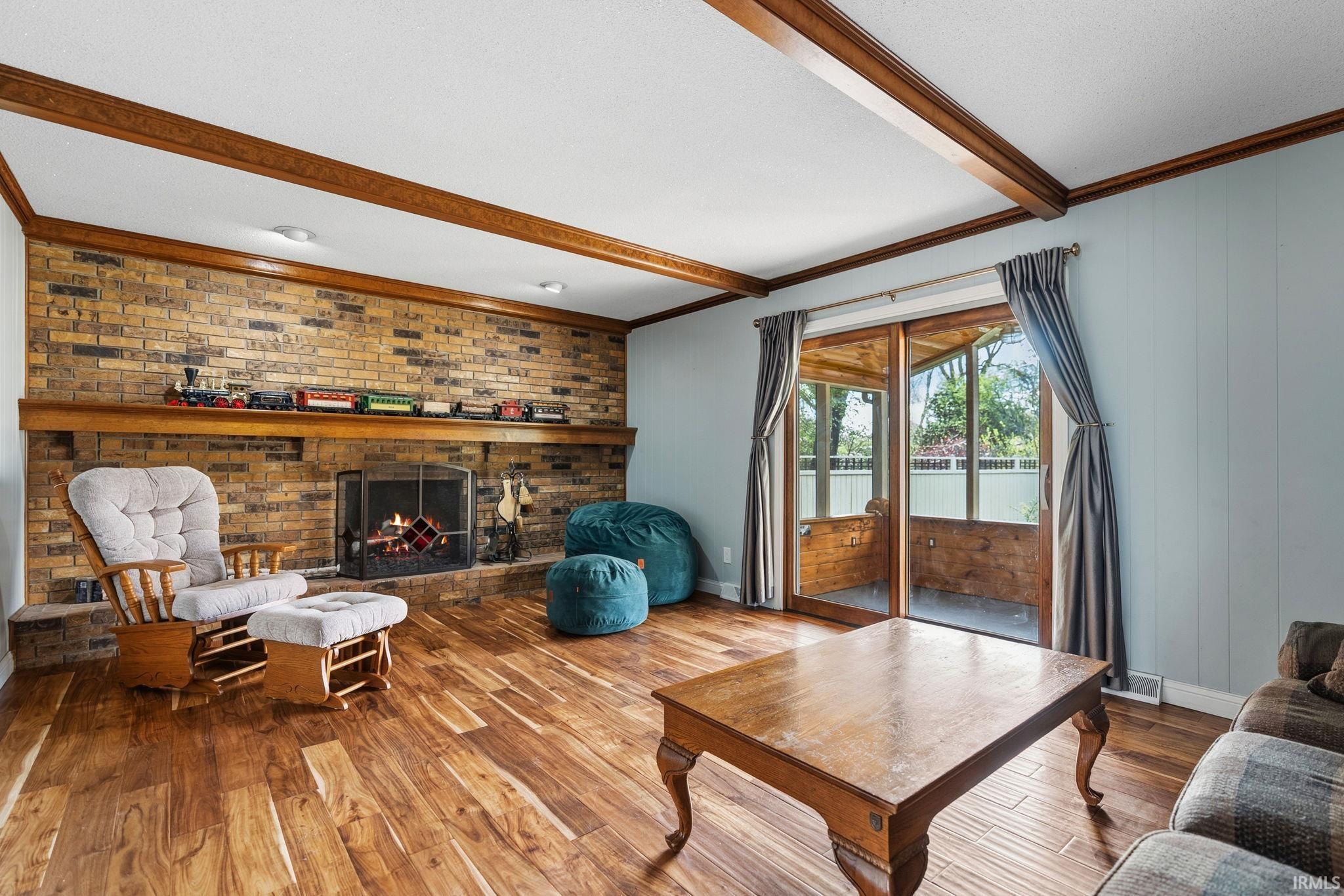 Living room with wood-type flooring, a fireplace, ornamental molding, and beam ceiling