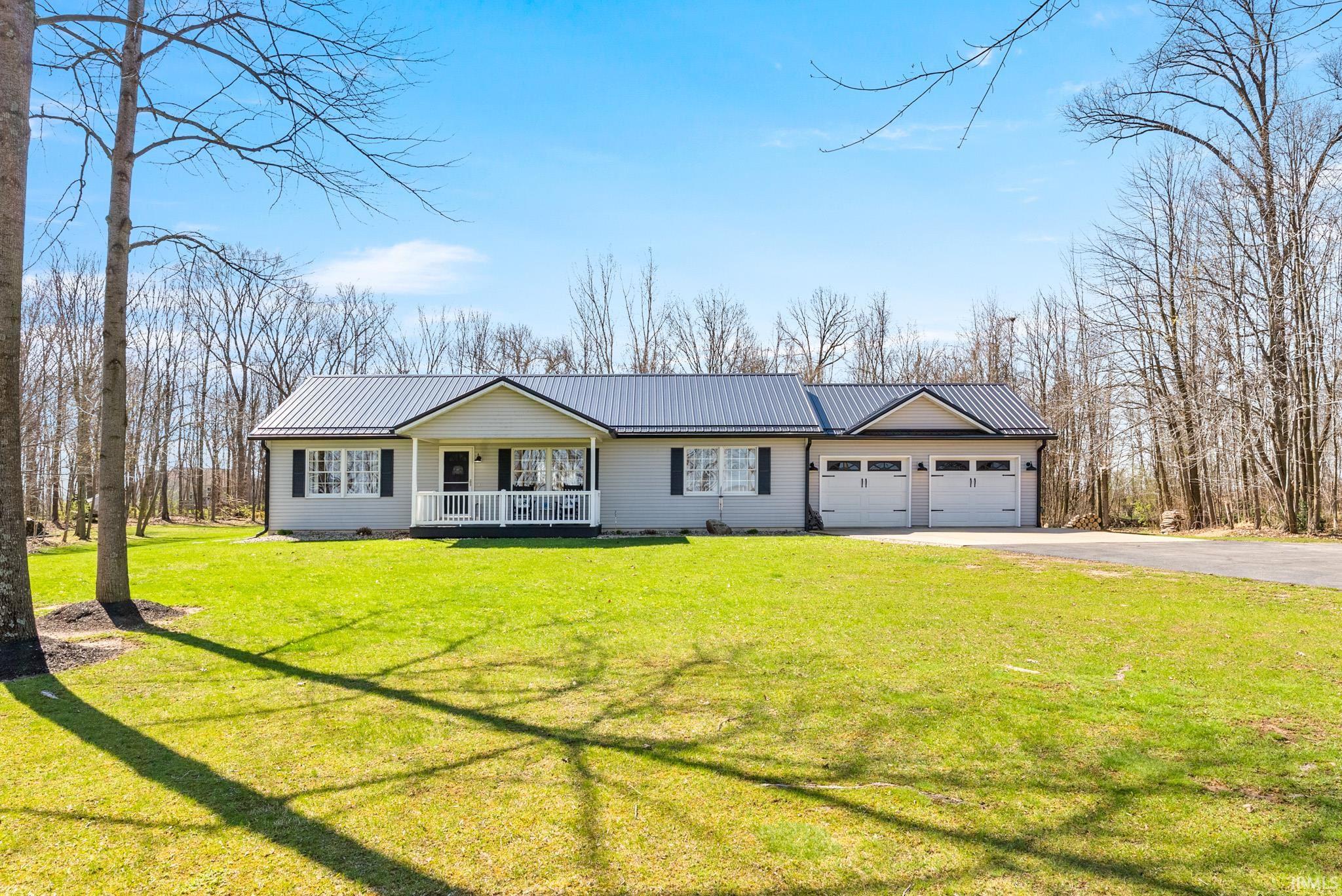 Ranch-style house featuring covered porch, a metal roof, a front yard, driveway, and an attached garage
