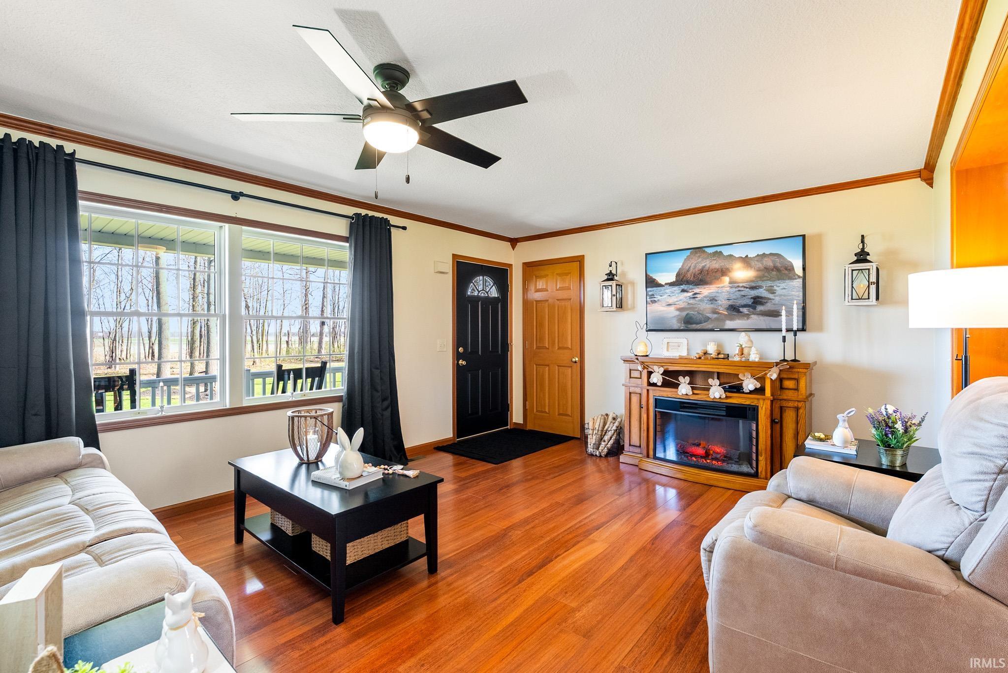 Living area with wood finished floors, a ceiling fan, a glass covered fireplace, and crown molding