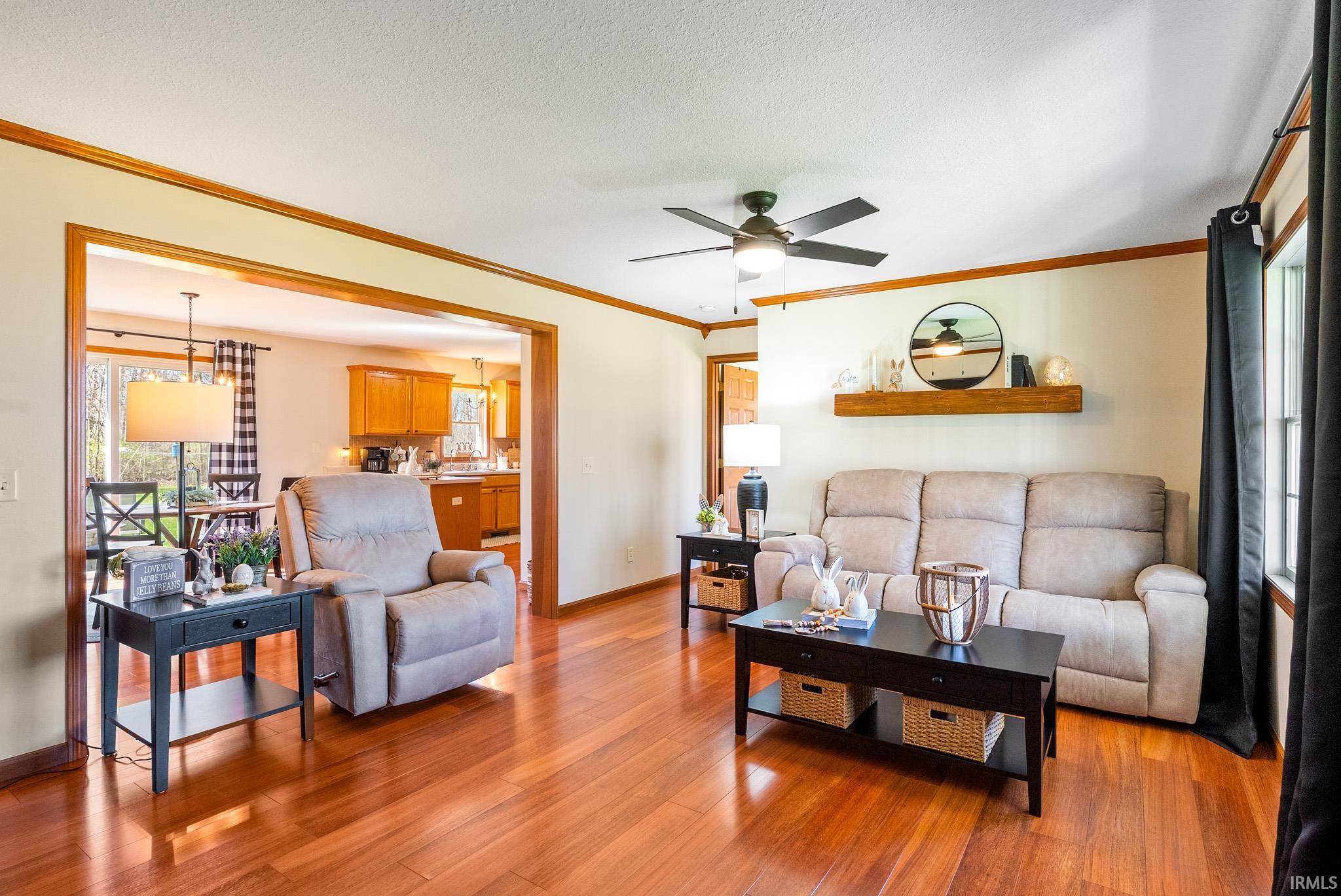 Living room featuring ceiling fan, light wood finished floors, ornamental molding, and a textured ceiling