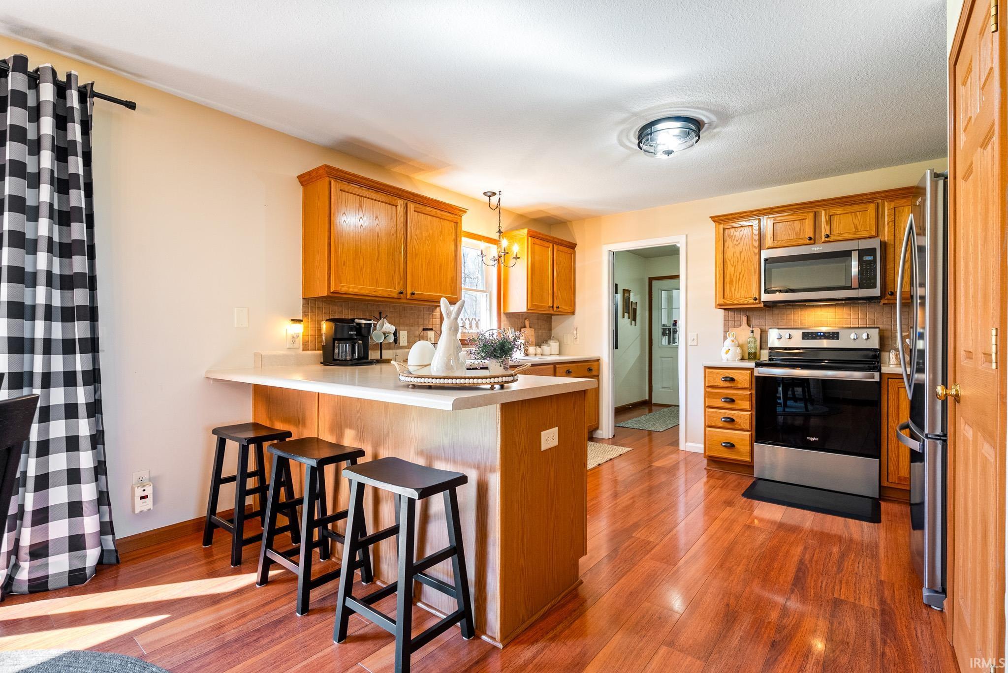 Kitchen featuring a breakfast bar area, a peninsula, stainless steel appliances, light countertops, and backsplash