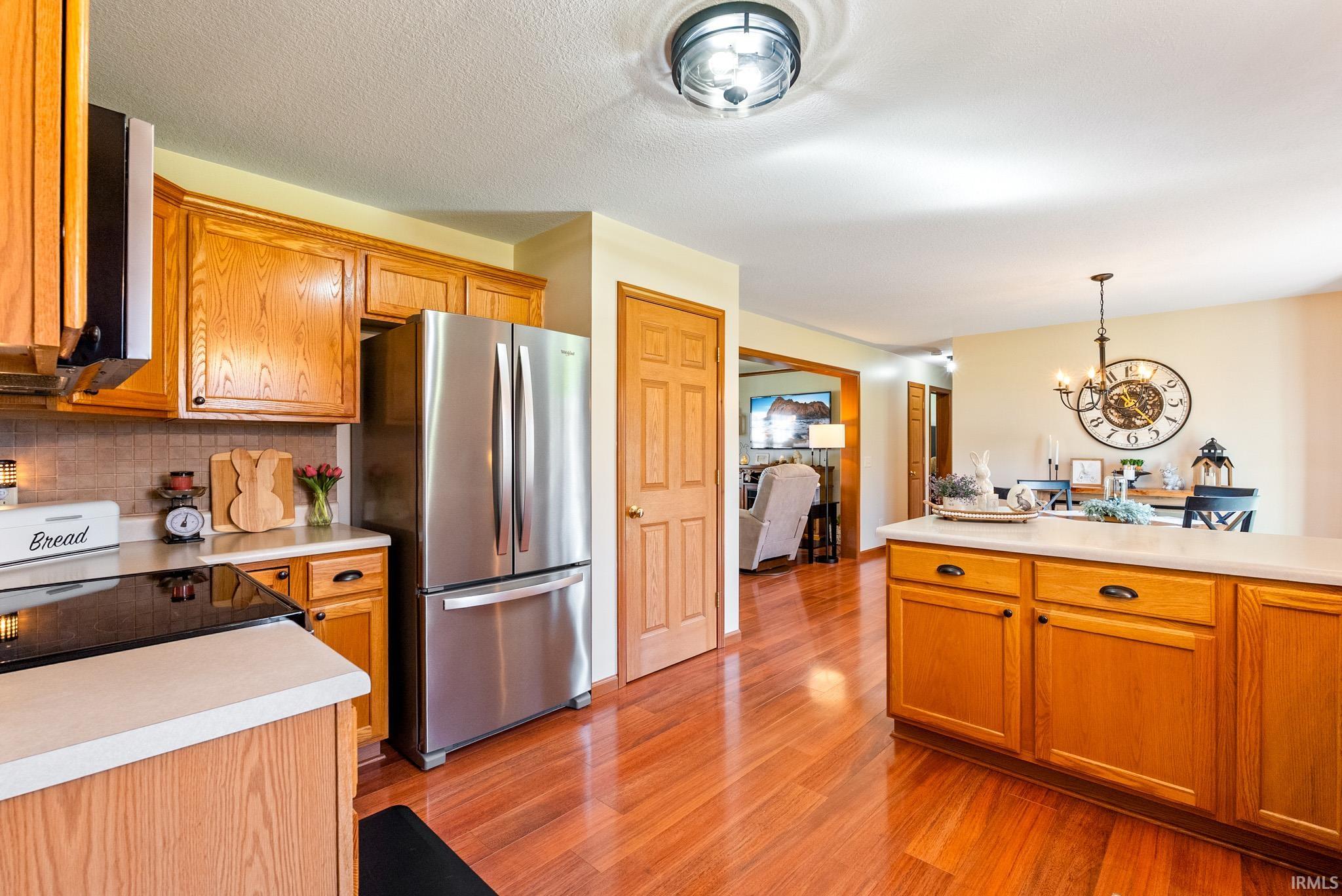 Kitchen featuring light countertops, freestanding refrigerator, wood finish cabinetry, hanging lights, and light wood finished floors