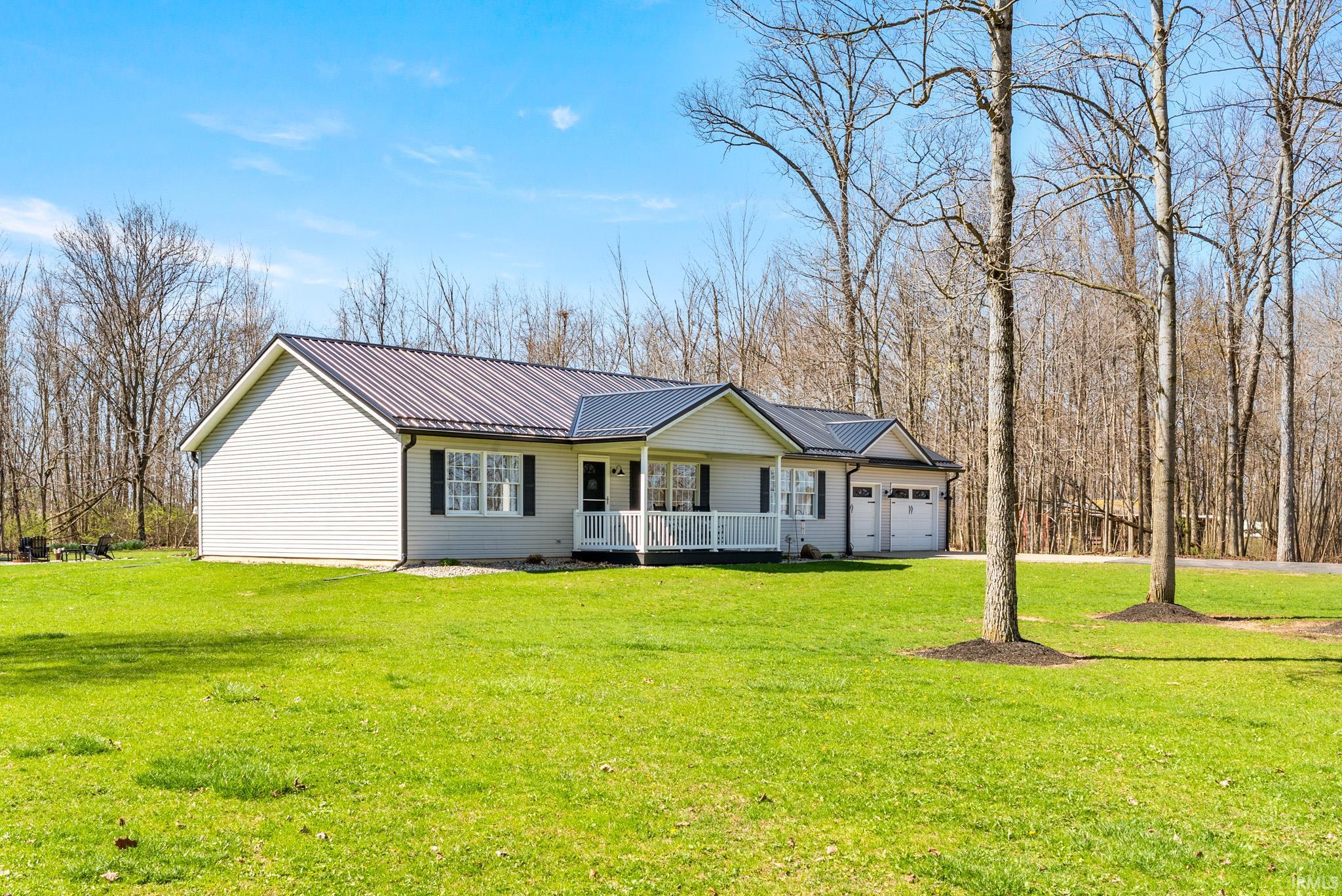 Ranch-style house featuring a porch, a metal roof, a front lawn, and an attached garage