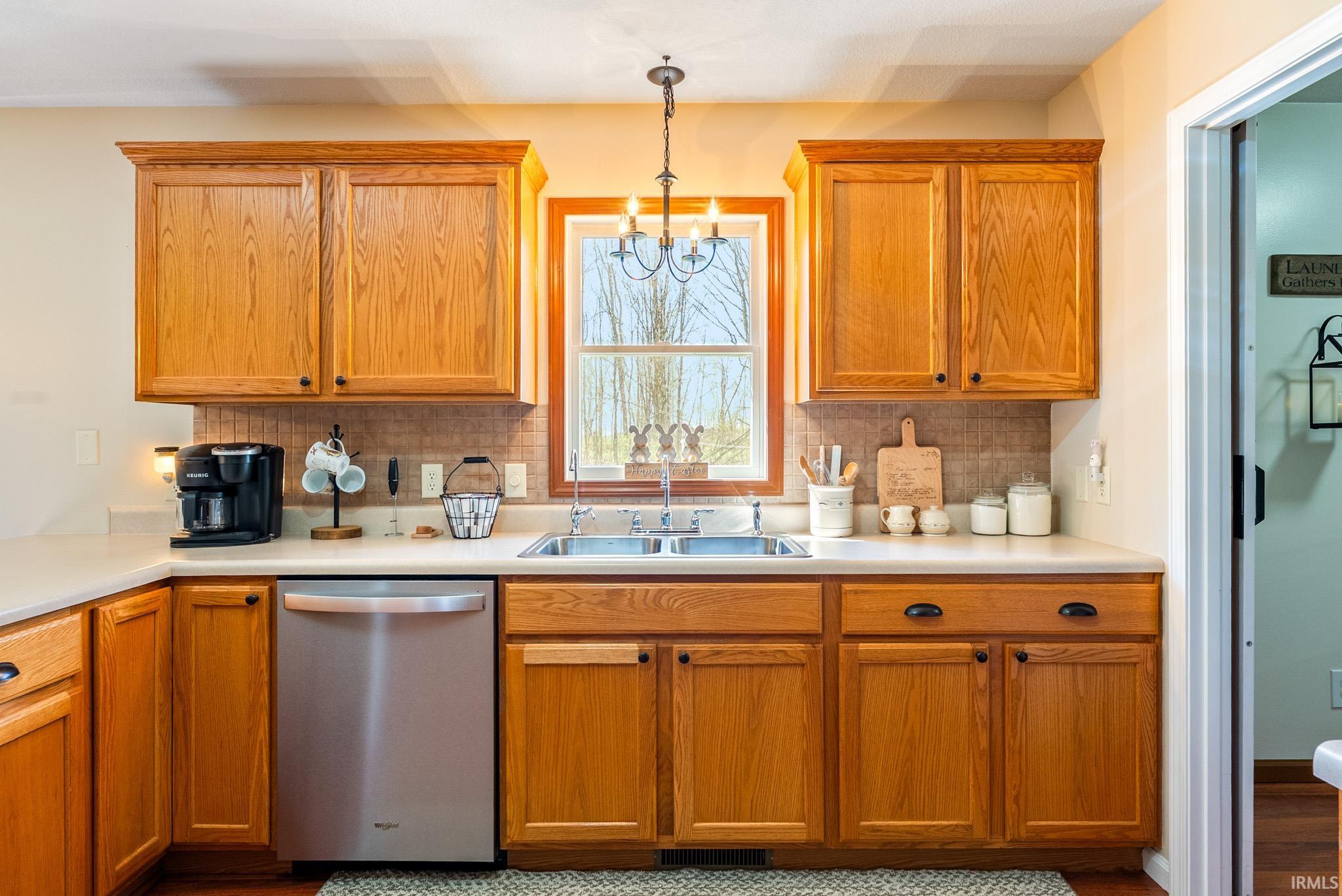 Kitchen featuring stainless steel dishwasher, hanging lights, wood finish cabinetry, light countertops, and tasteful backsplash