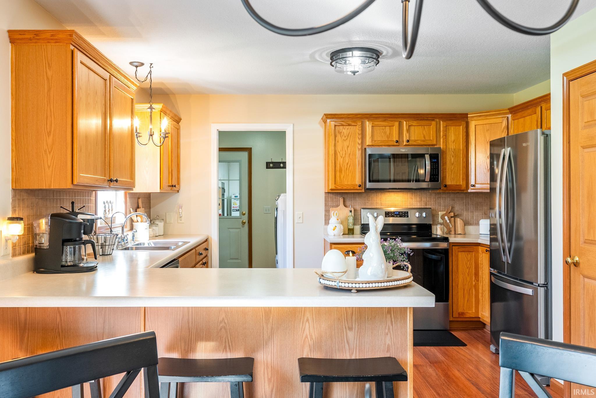 Kitchen with a breakfast bar, stainless steel appliances, light countertops, decorative backsplash, and a peninsula
