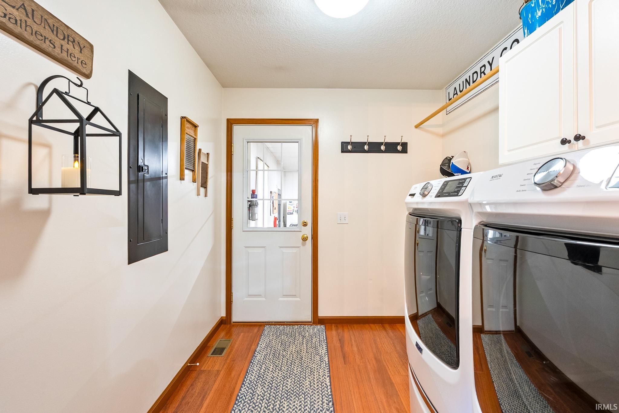 Laundry area featuring electric panel, separate washer and dryer, light wood-style flooring, a textured ceiling, and cabinet space