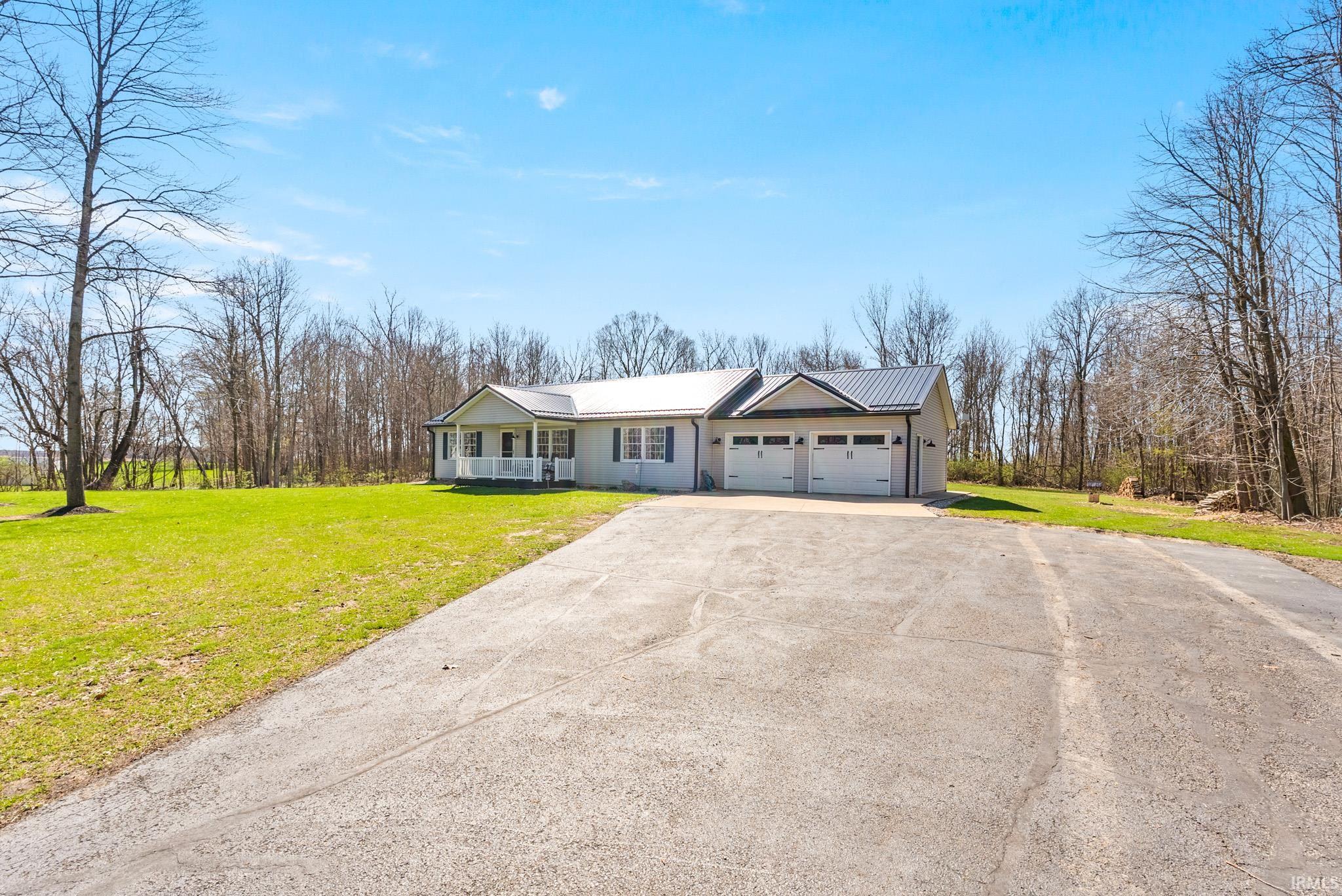 Ranch-style house featuring a front yard, concrete driveway, a garage, a metal roof, and a porch