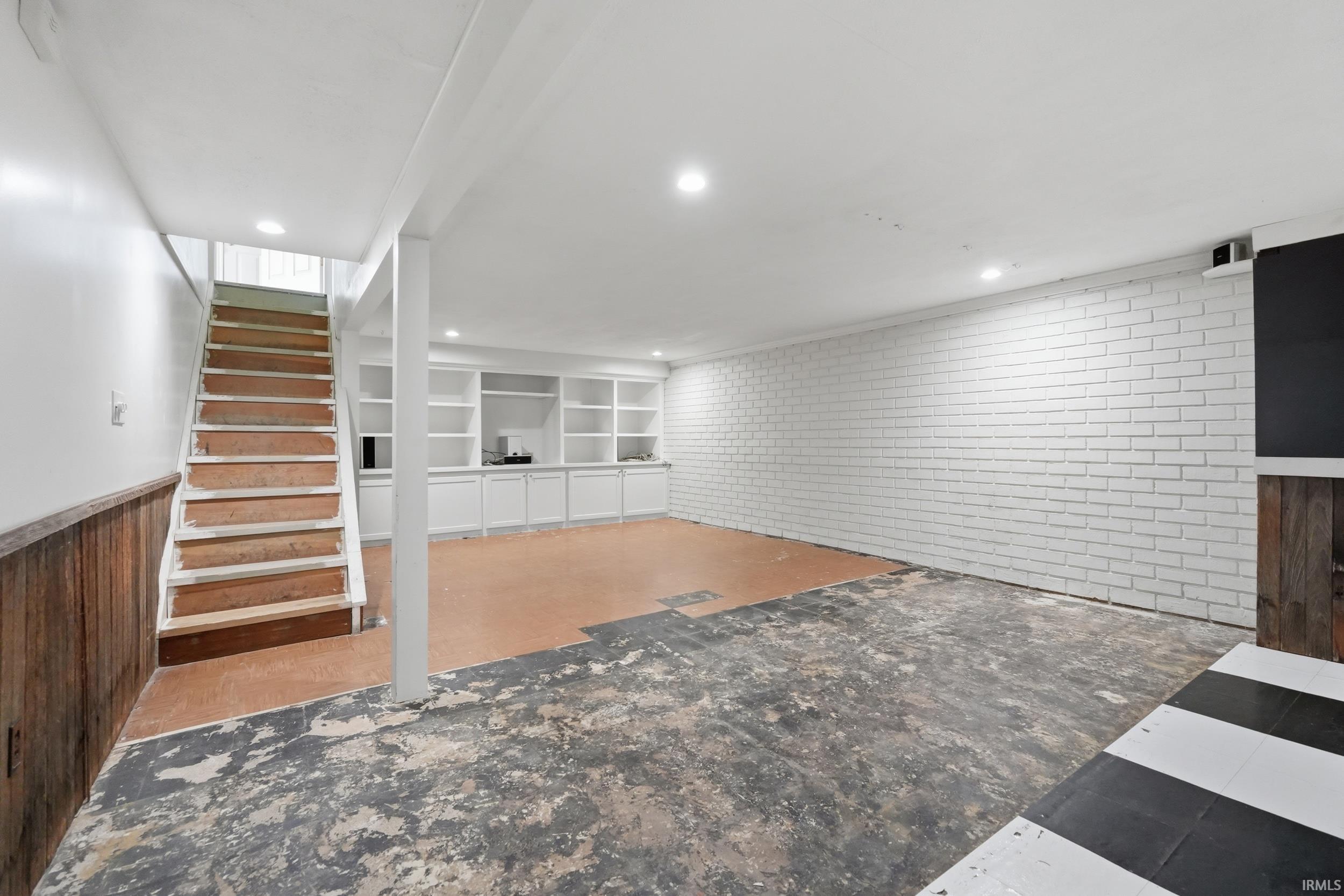 Finished basement featuring brick wall, a wainscoted wall, built in features, recessed lighting, and wooden walls