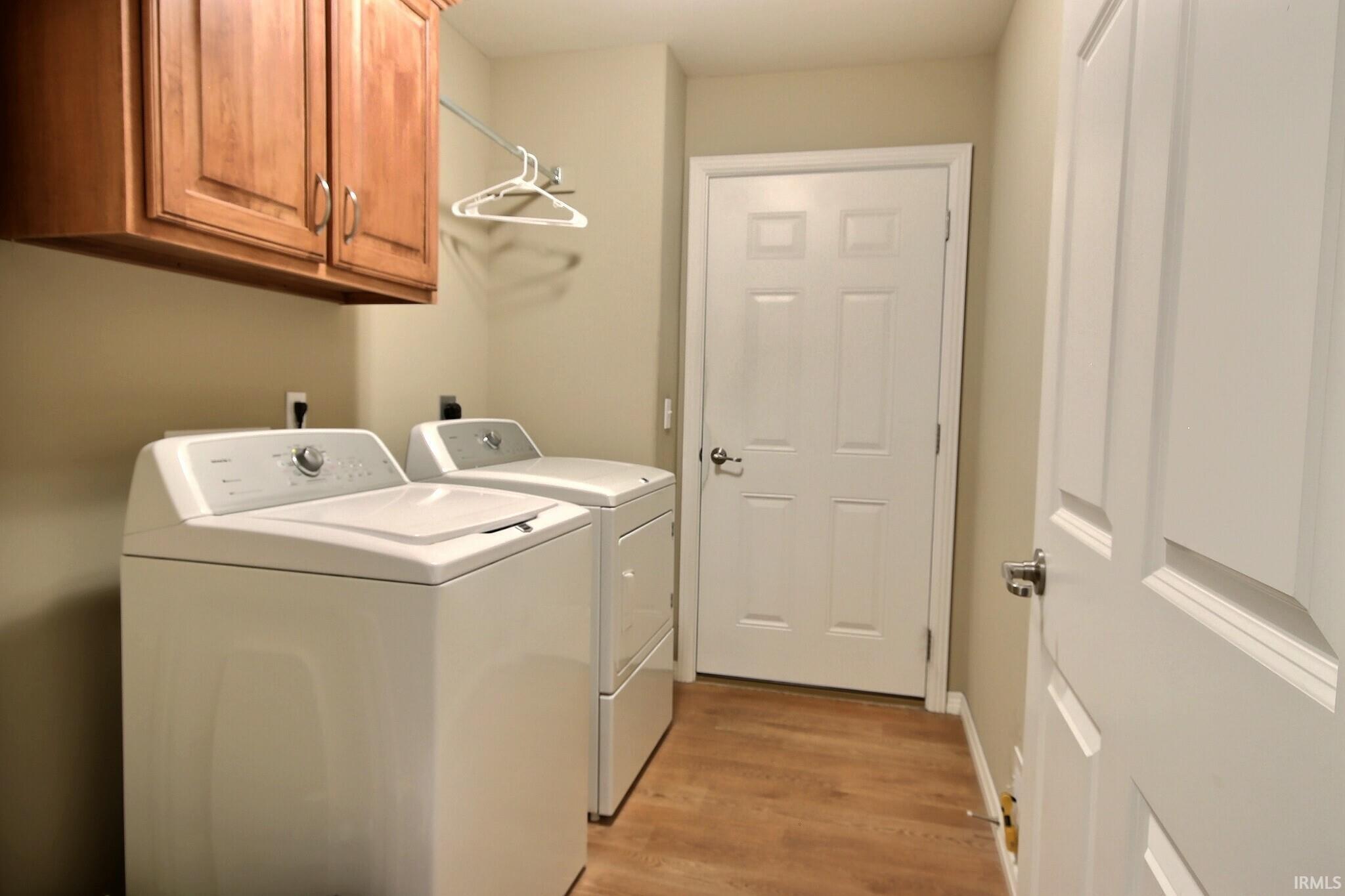 Laundry area with separate washer and dryer, light wood-style floors, and cabinet space