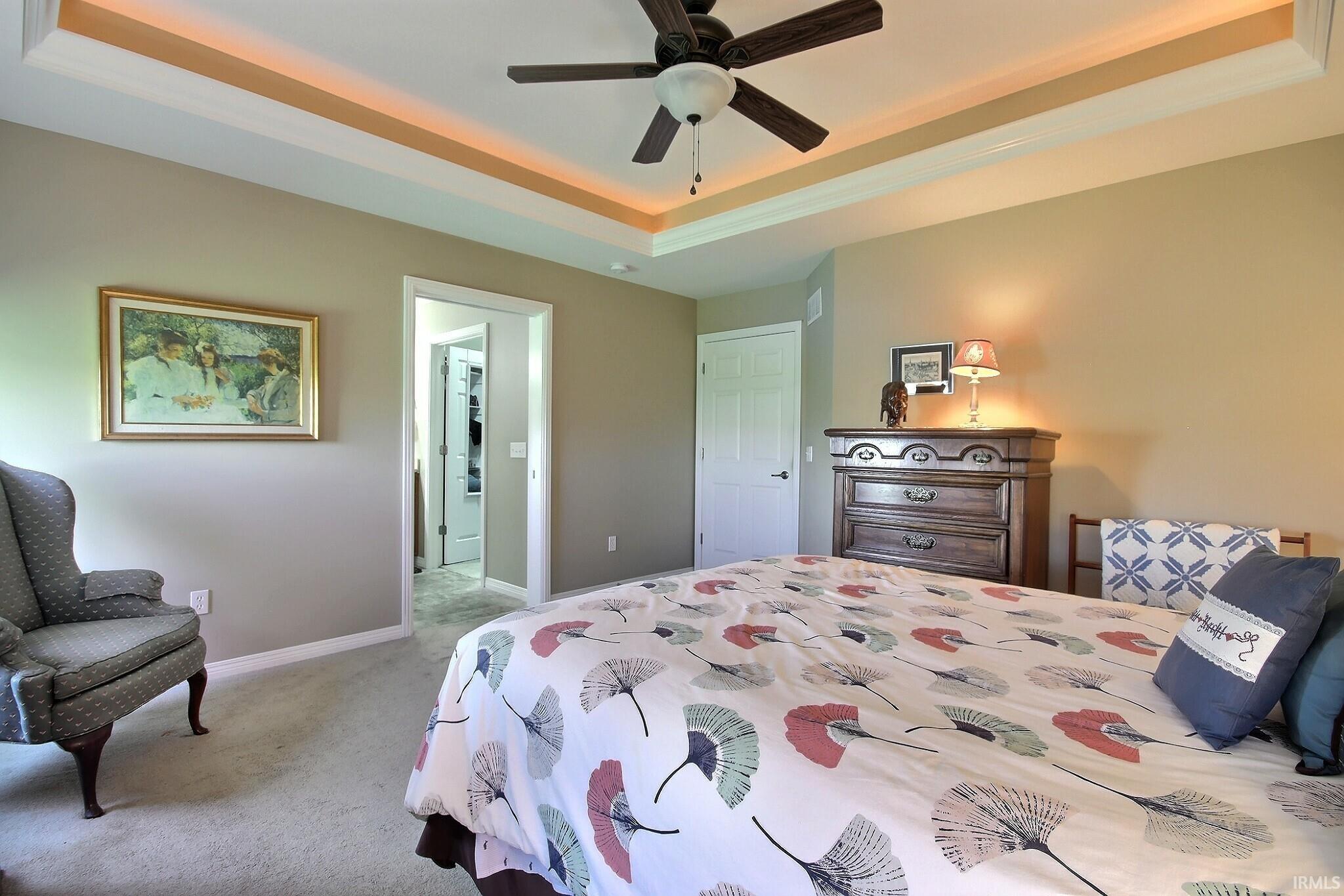 Bedroom with a tray ceiling, light colored carpet, and ceiling fan