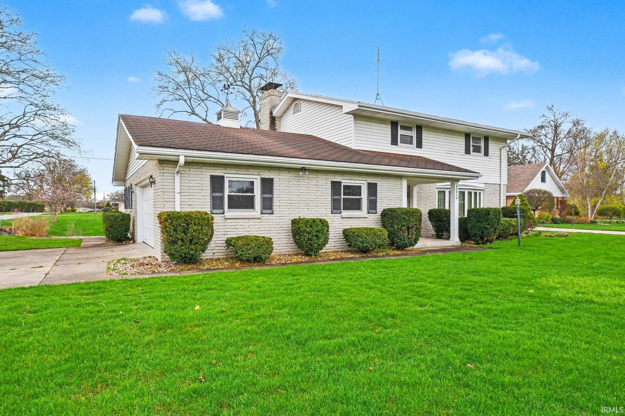 Traditional-style house with a front yard, driveway, a chimney, a garage, and brick siding