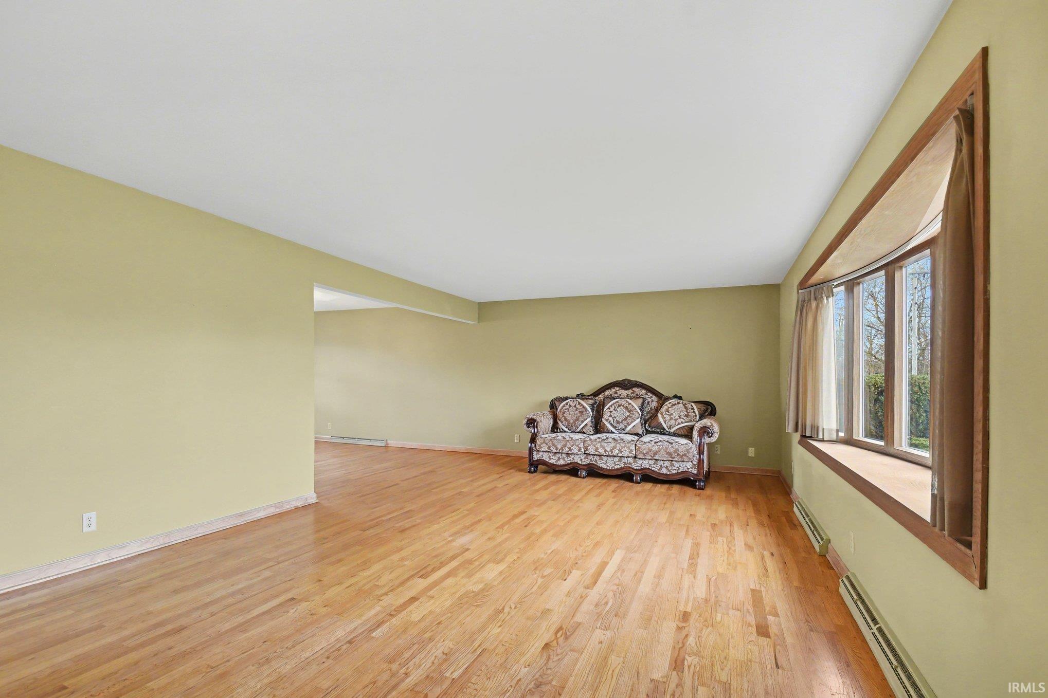 Living area with a baseboard heating unit, light wood finished floors, and a baseboard radiator