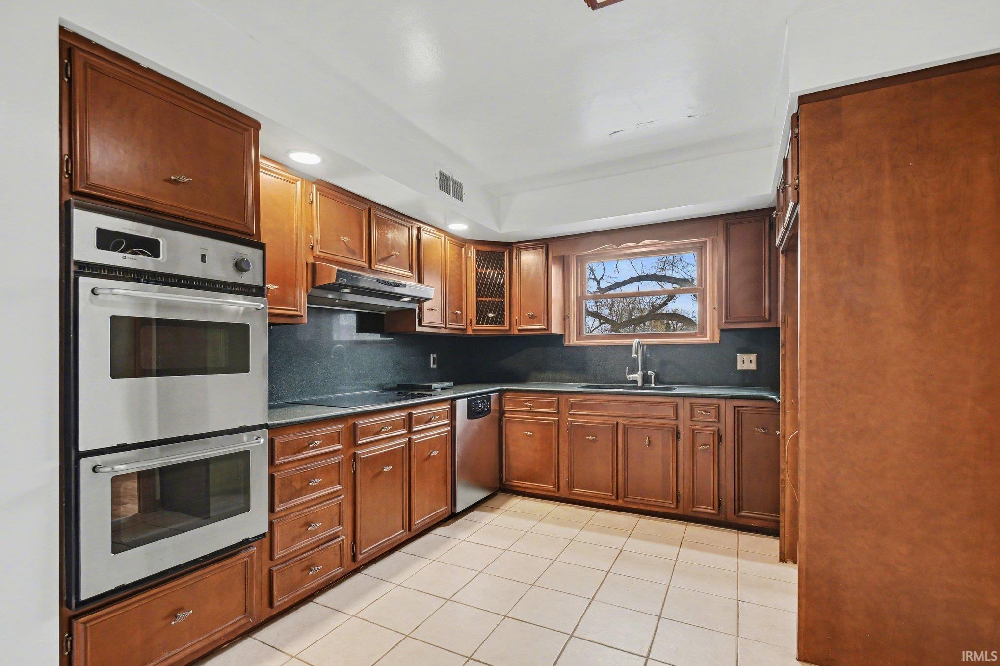 Kitchen featuring stainless steel appliances, wood finish cabinetry, tasteful backsplash, light tile patterned flooring, and recessed lighting