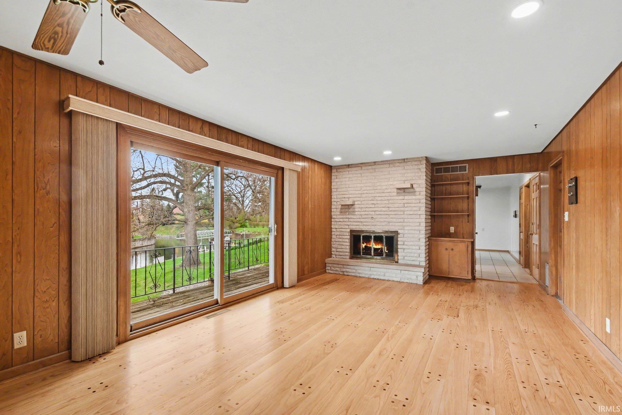 Unfurnished living room with wooden walls, recessed lighting, light wood-type flooring, a fireplace, and ceiling fan