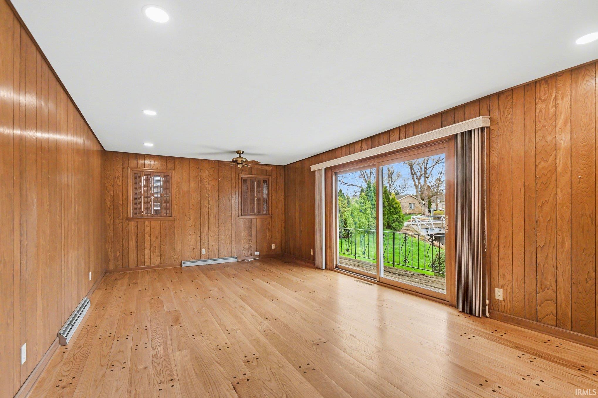 Empty room with recessed lighting, a ceiling fan, light wood-type flooring, wood walls, and a baseboard radiator