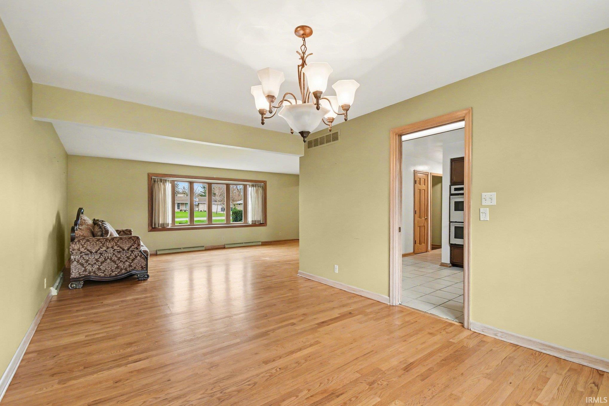 Empty room with a chandelier, light wood-type flooring, and a baseboard heating unit