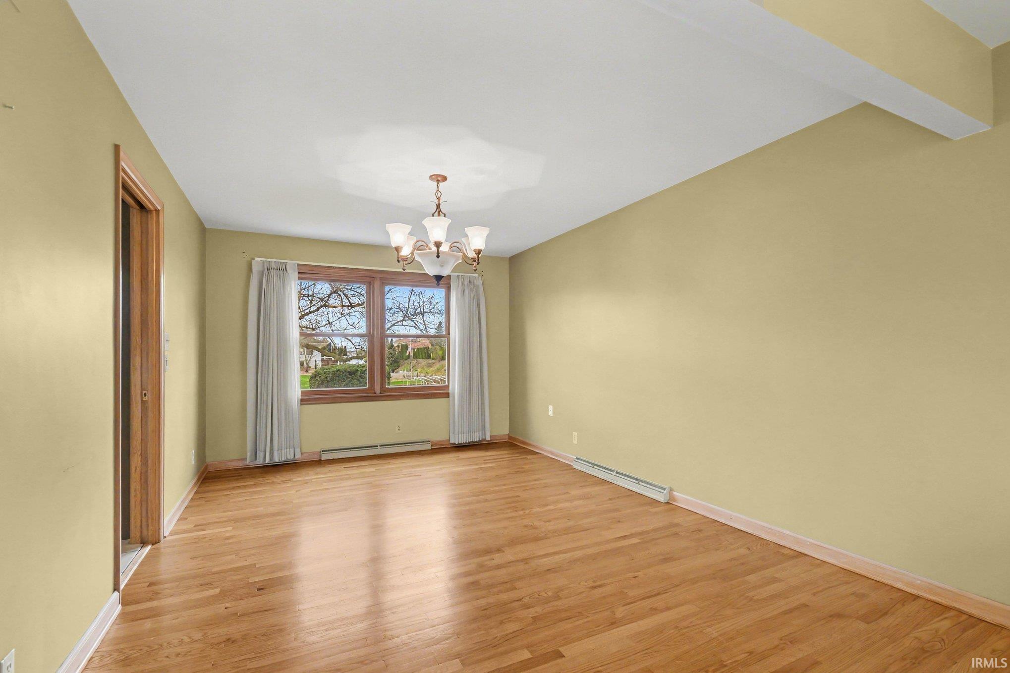 Spare room featuring a chandelier, light wood finished floors, and a baseboard heating unit