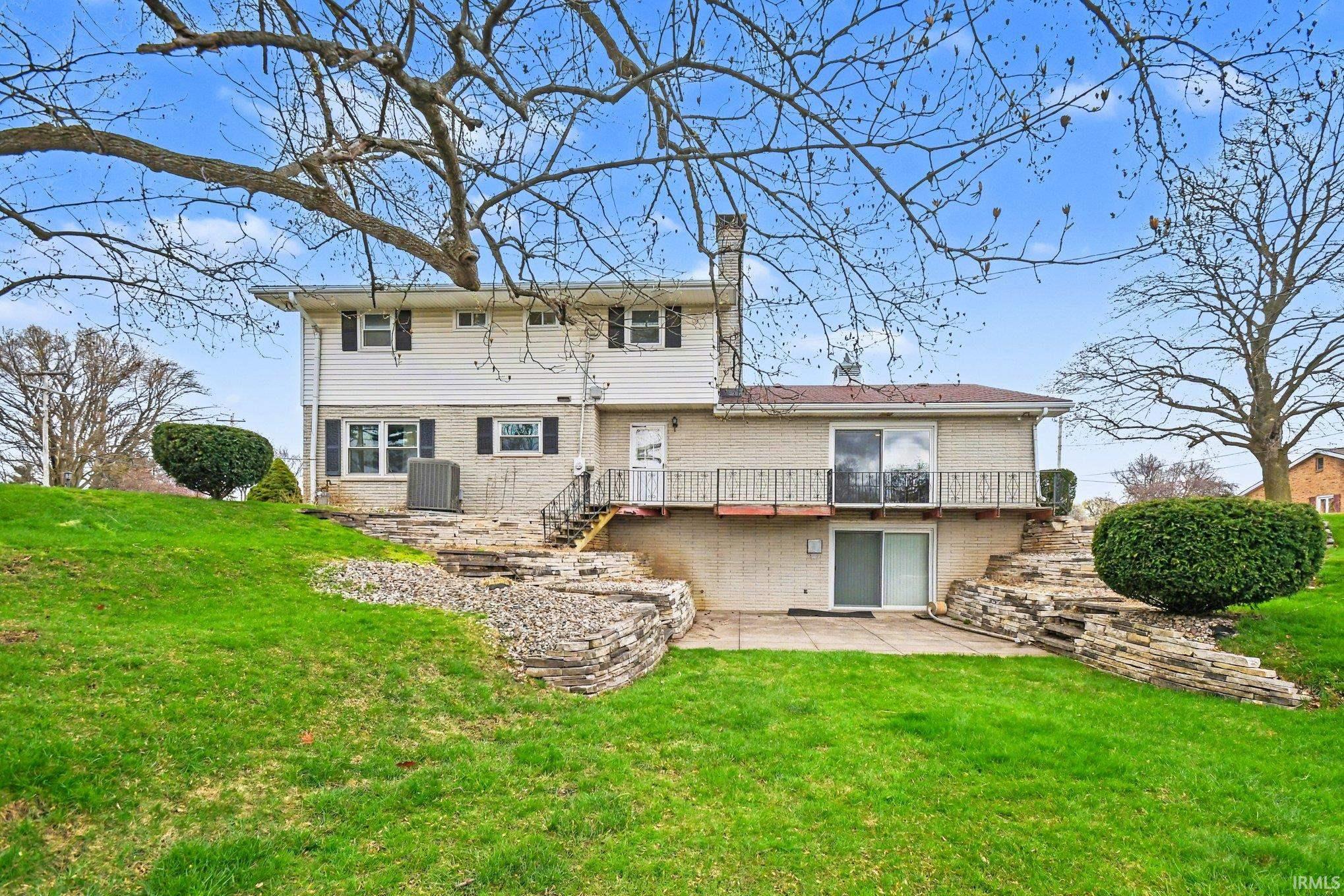 Rear view of house featuring a patio, a lawn, a chimney, and brick siding