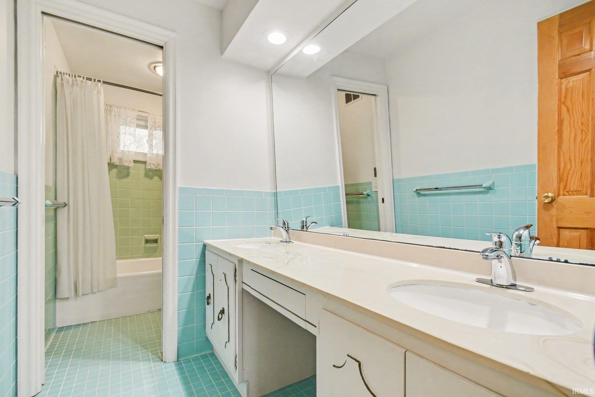 Full bathroom with double vanity, shower / bathtub combination with curtain, tile walls, a wainscoted wall, and recessed lighting