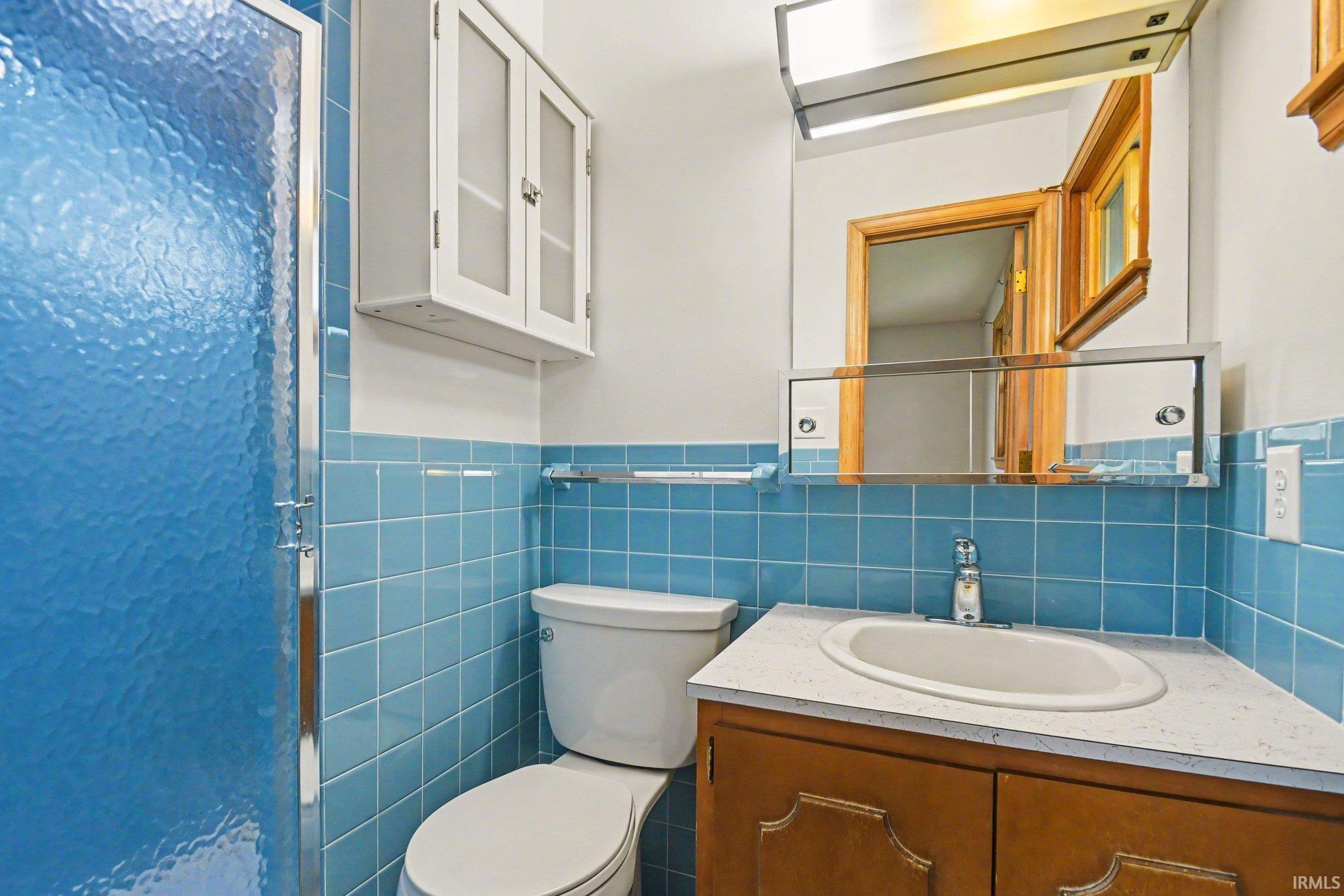 Bathroom featuring a shower, vanity, tile walls, and wainscoting