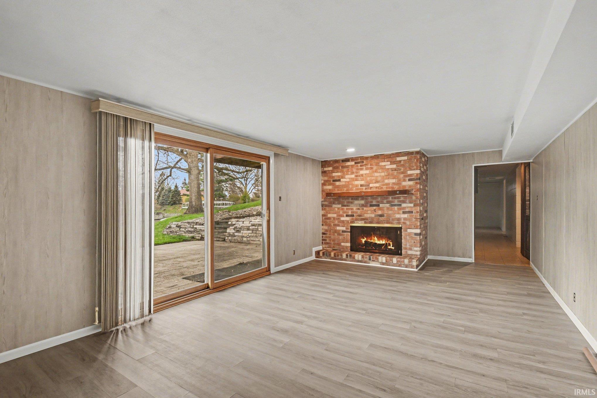 Unfurnished living room with light wood-style floors, a fireplace, and wood walls