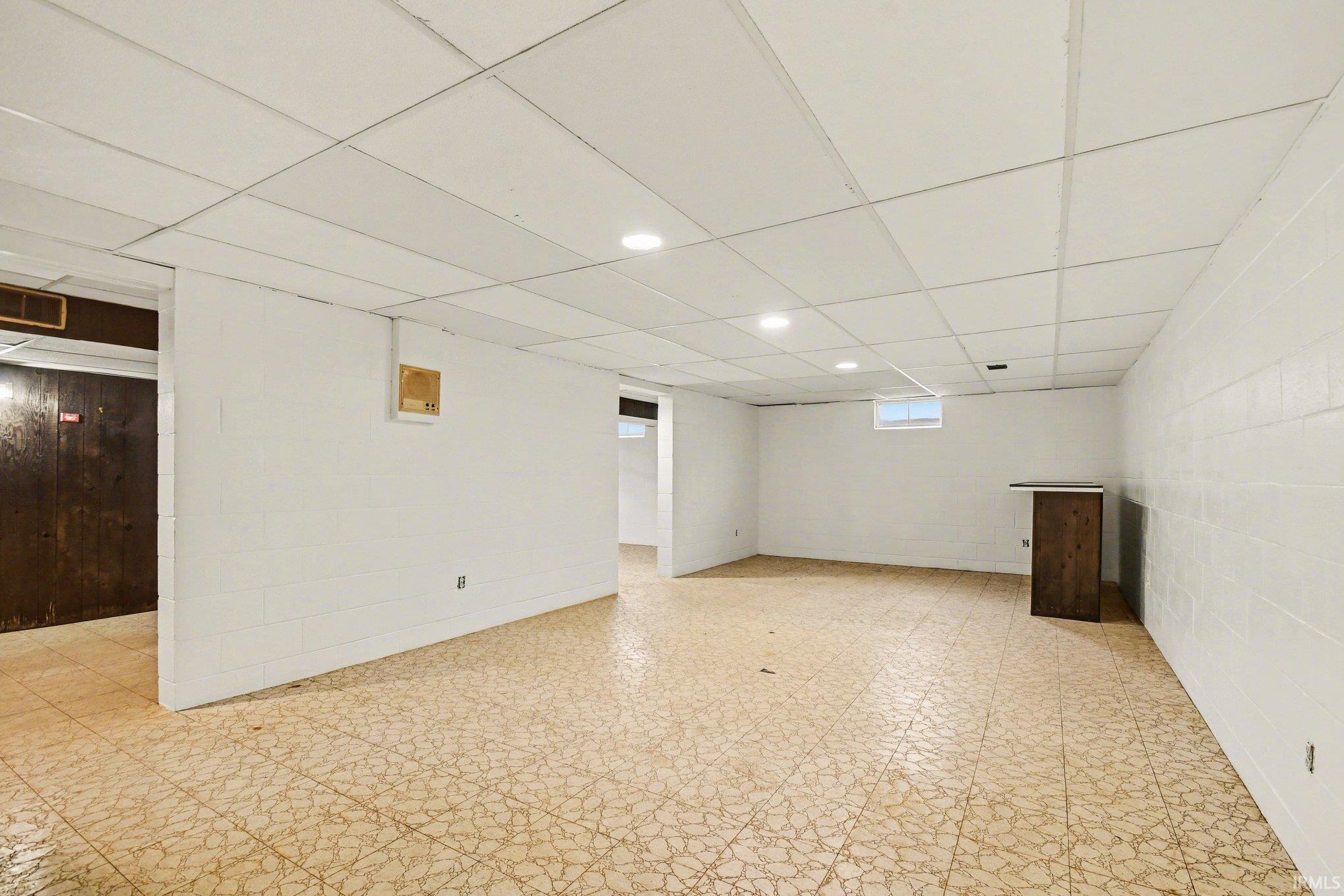 Basement with a drop ceiling, light flooring, concrete block wall, and recessed lighting