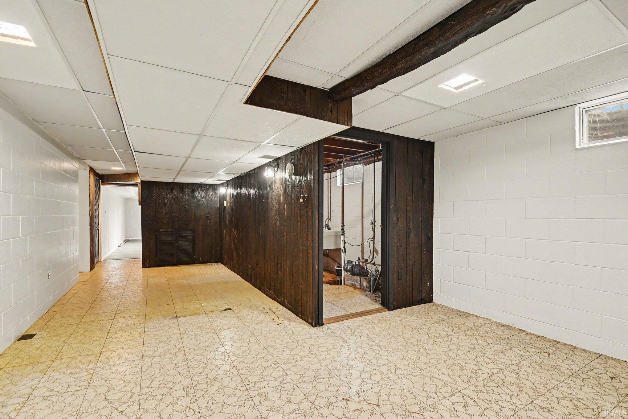 Finished basement featuring light flooring, concrete block wall, and a drop ceiling