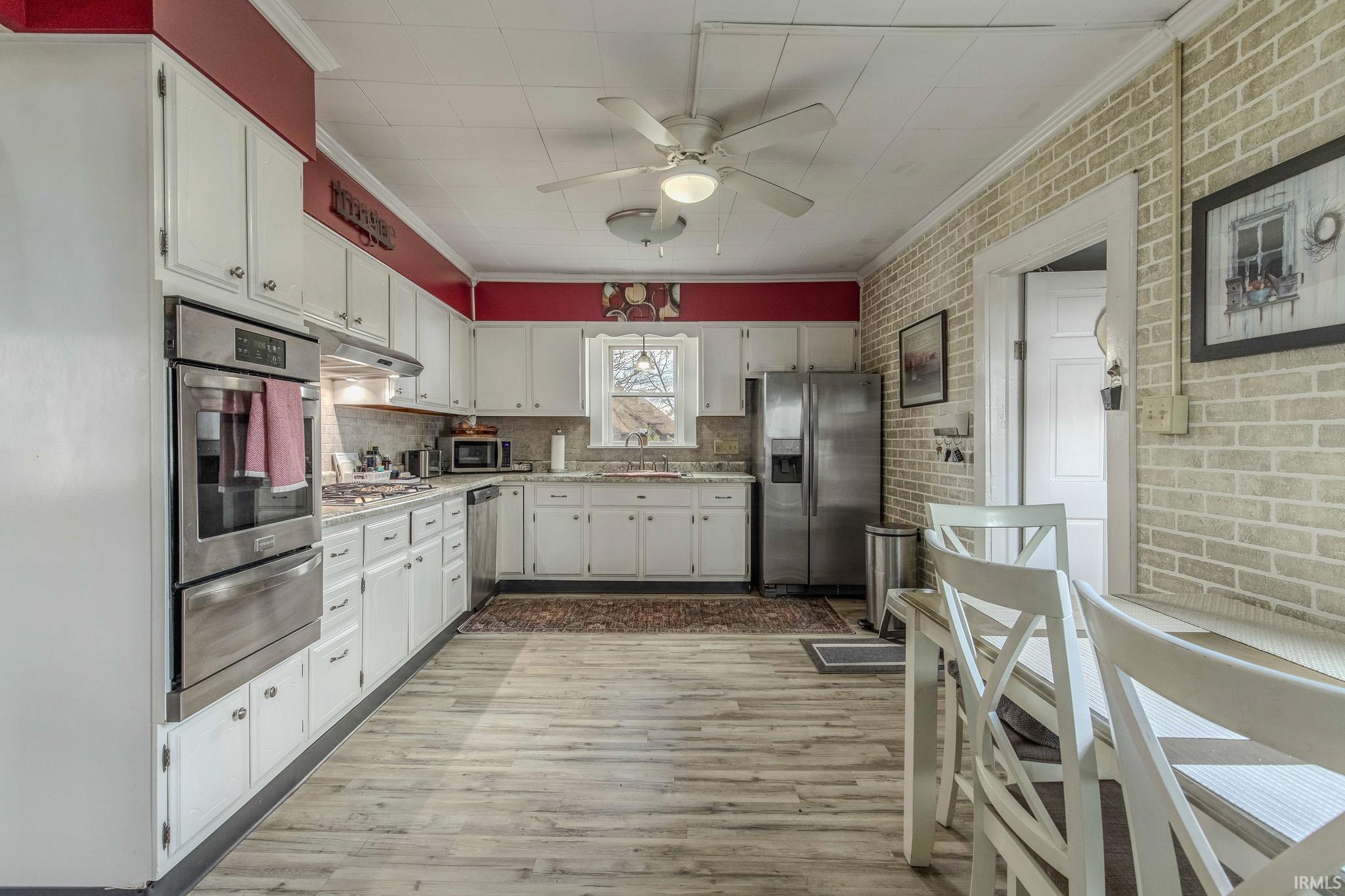 Kitchen with ornamental molding, a ceiling fan, stainless steel appliances, light wood-style flooring, and a warming drawer