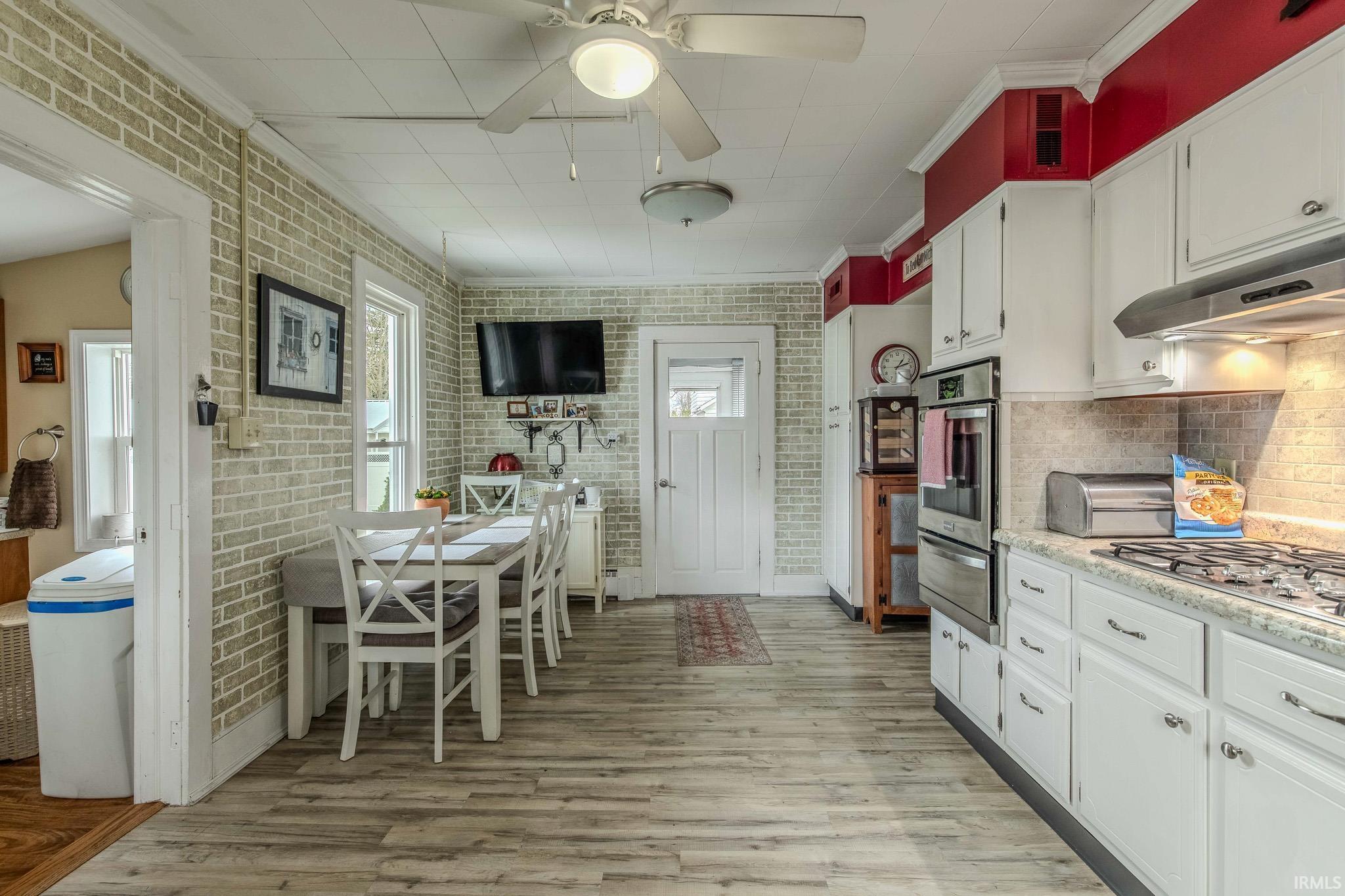 Kitchen with brick wall, crown molding, white cabinetry, ceiling fan, and stainless steel appliances