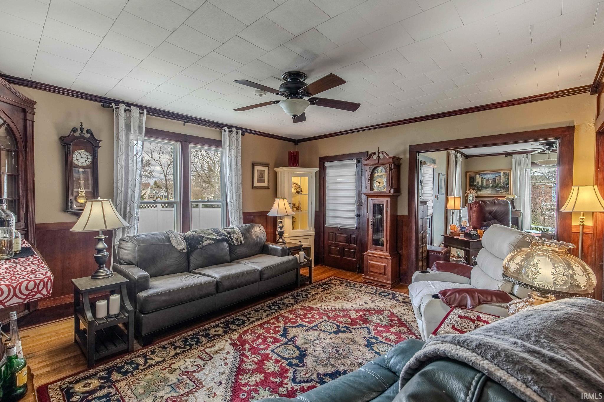 Living area with wainscoting, crown molding, wooden walls, ceiling fan, and wood finished floors