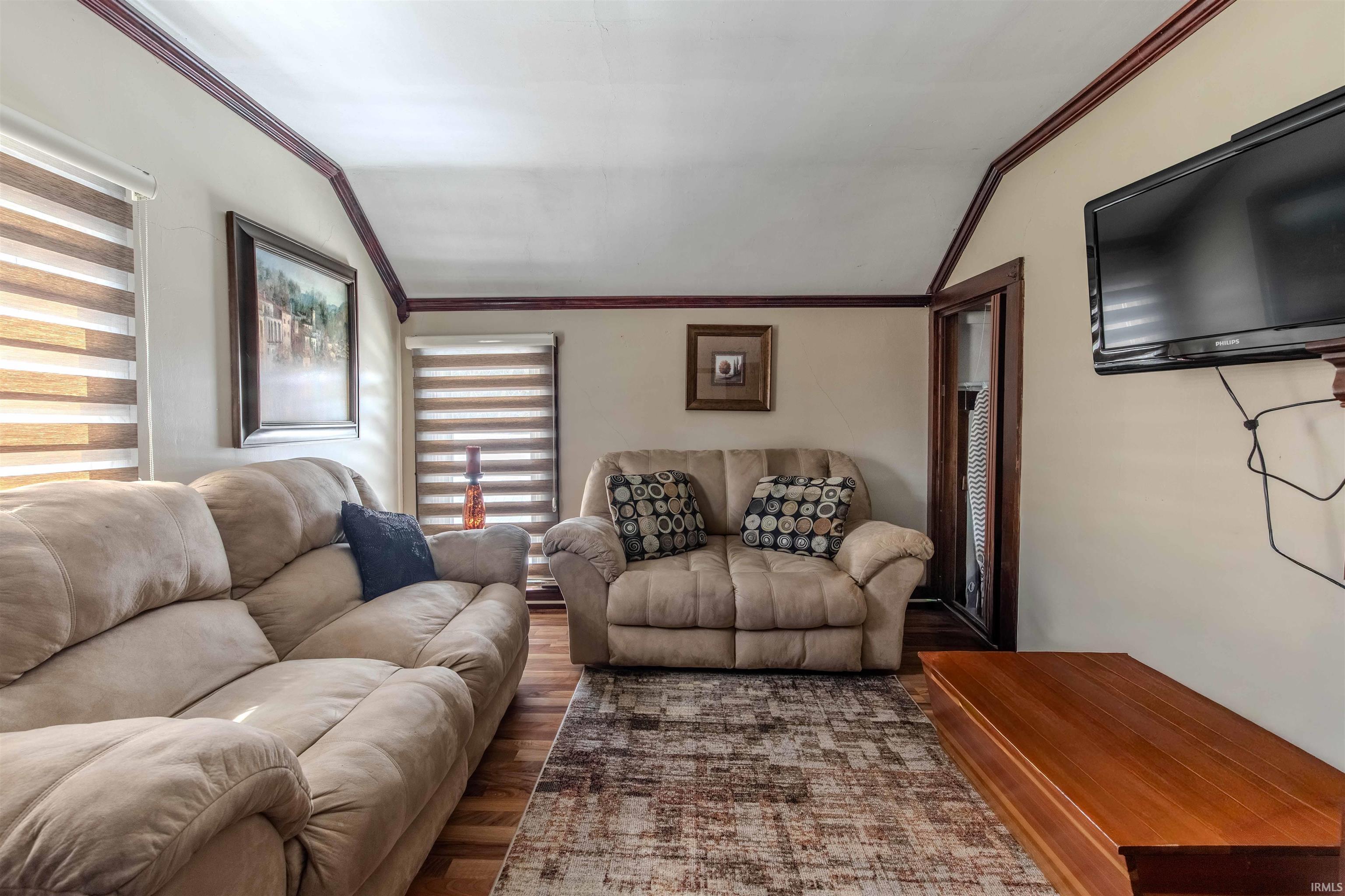 Living room with vaulted ceiling, ornamental molding, and wood finished floors