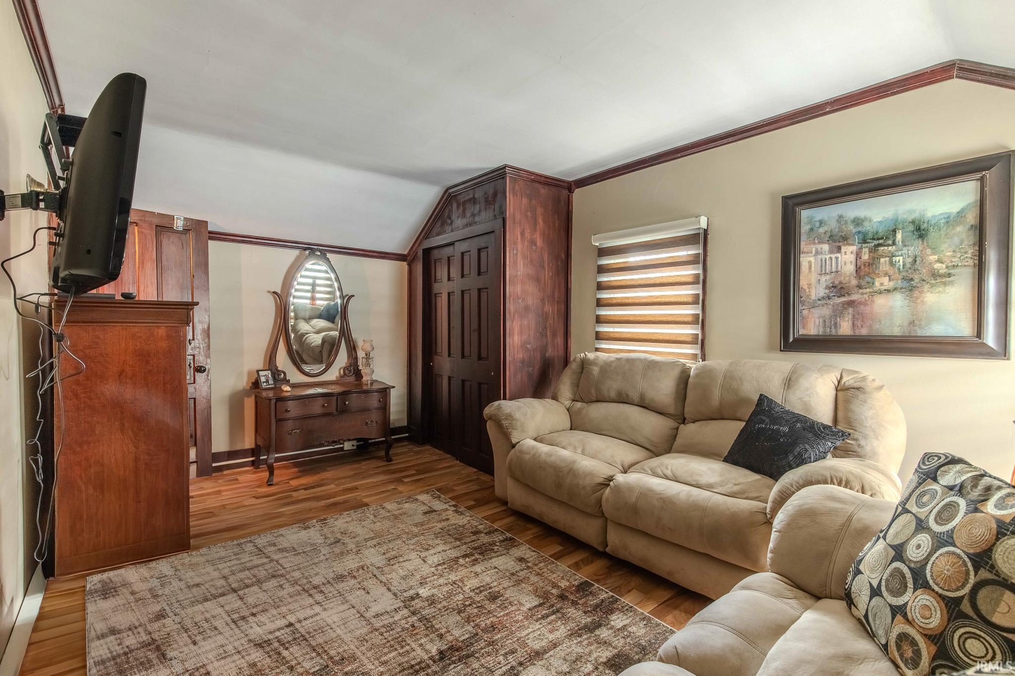 Living area featuring vaulted ceiling, ornamental molding, and wood finished floors