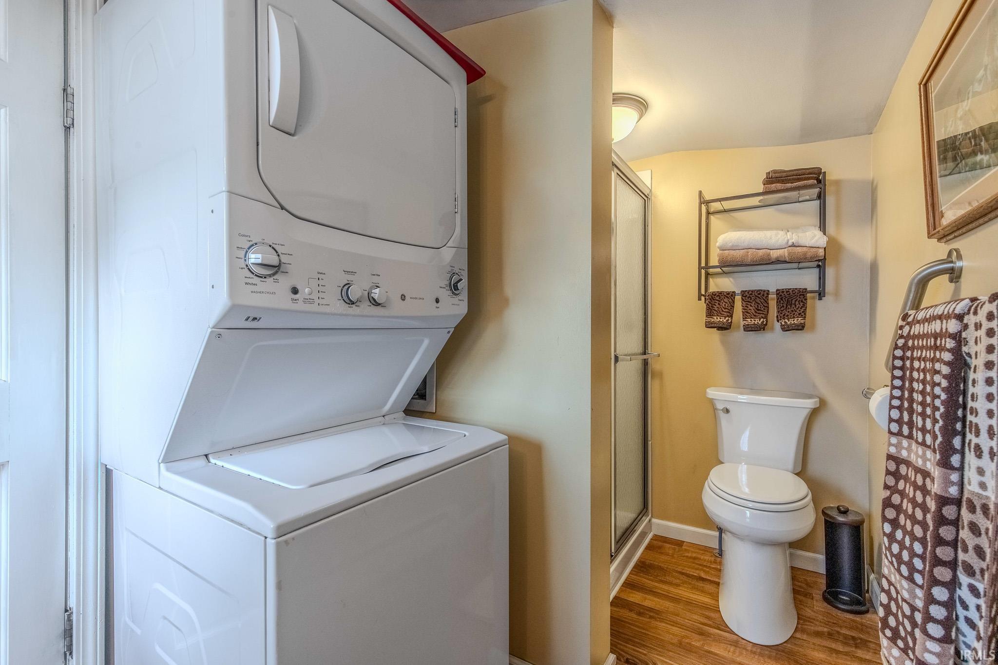 Full bathroom featuring a stall shower, light wood finished floors, and stacked washer and clothes dryer