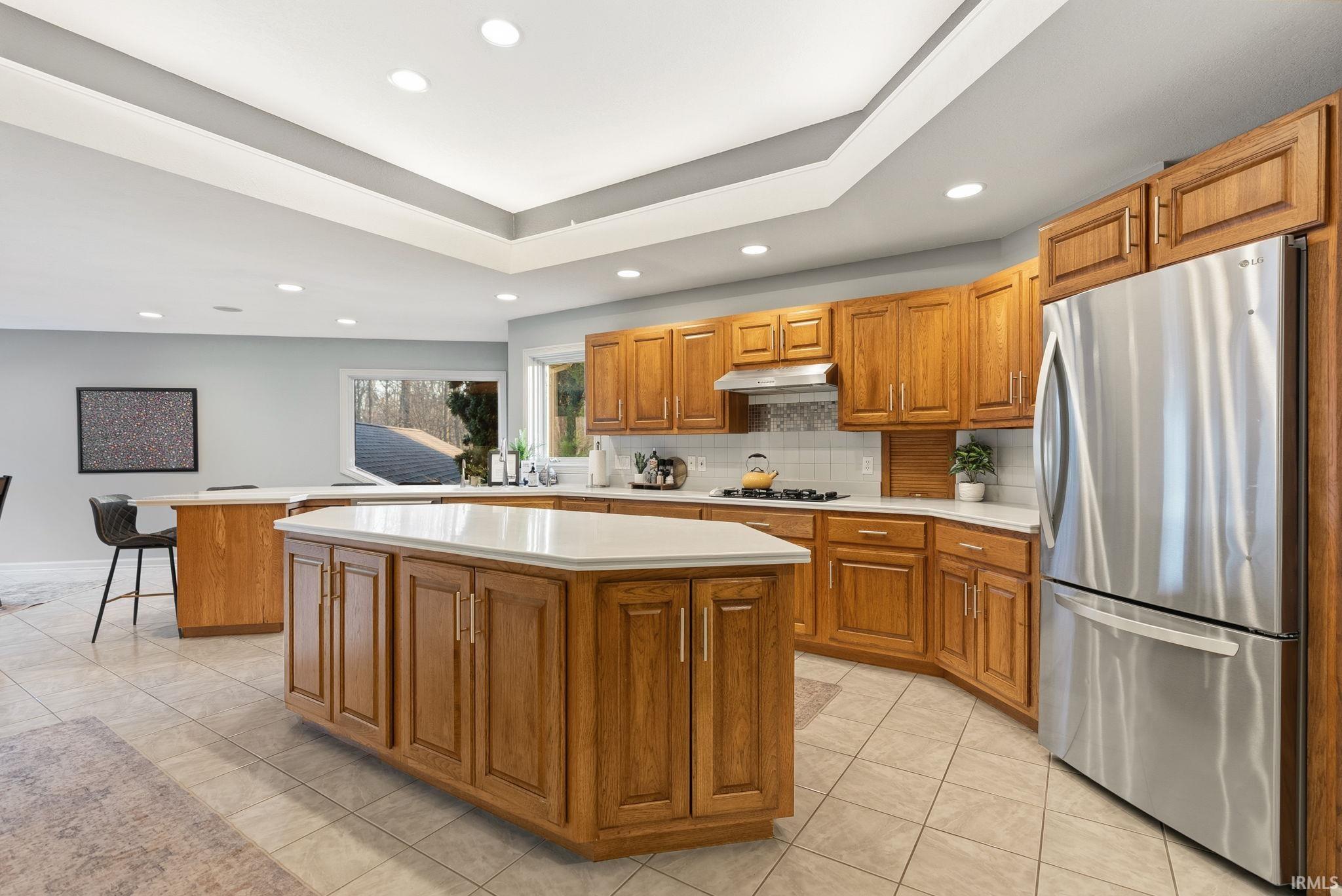 Kitchen featuring a center island, wood finish cabinets, freestanding refrigerator, light countertops, and a raised ceiling