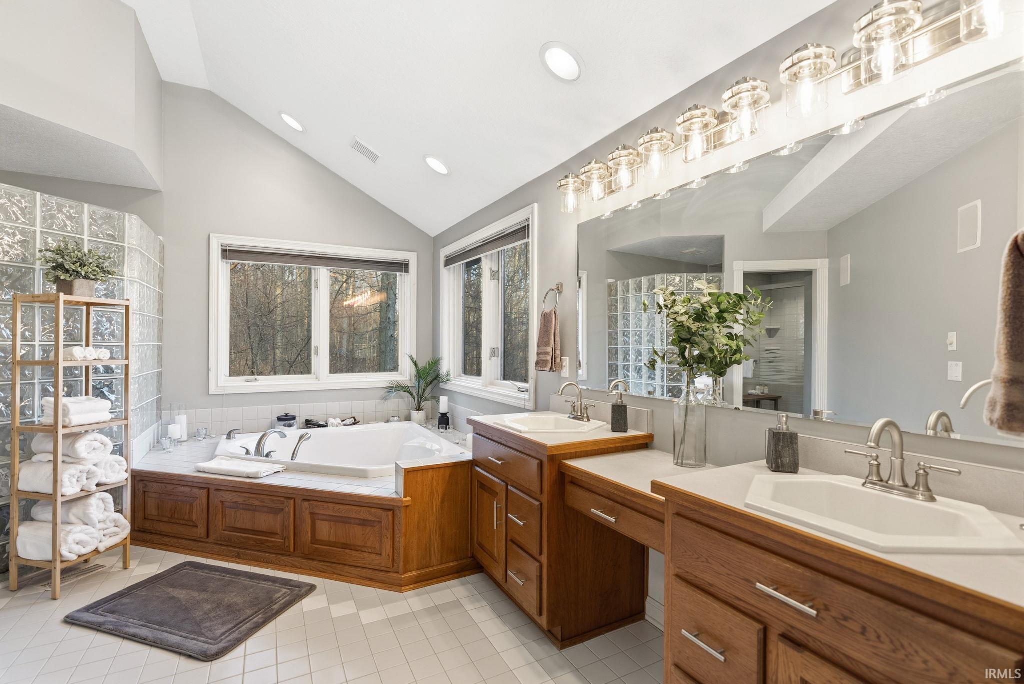 Bathroom featuring lofted ceiling, two vanities, a garden tub, walk in shower, and recessed lighting