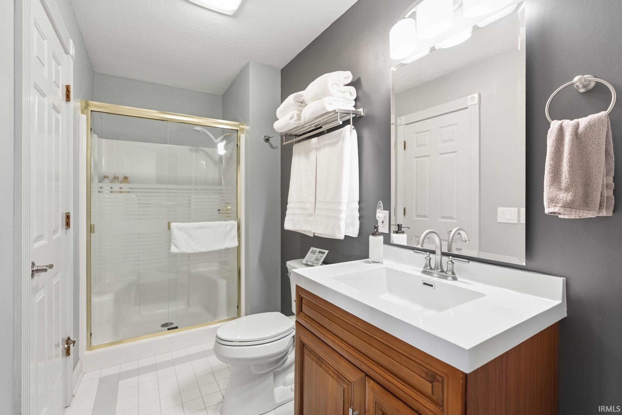 Full bath with vanity, a shower stall, light tile patterned flooring, and a textured ceiling