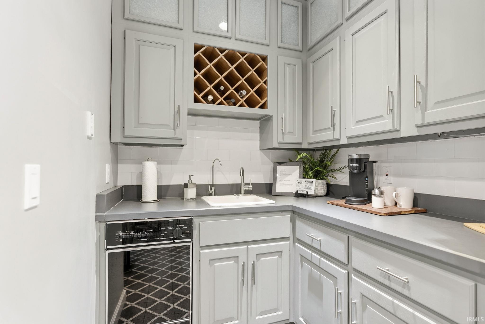 Kitchen featuring beverage cooler, light countertops, tasteful backsplash, and glass insert cabinets