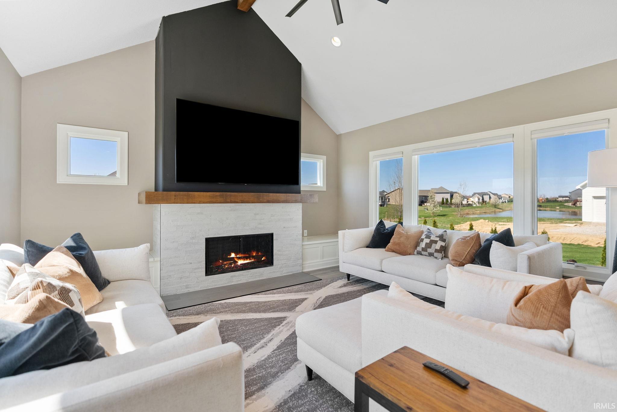Living room featuring a ceiling fan, a stone fireplace, a high ceiling, and wood finished floors