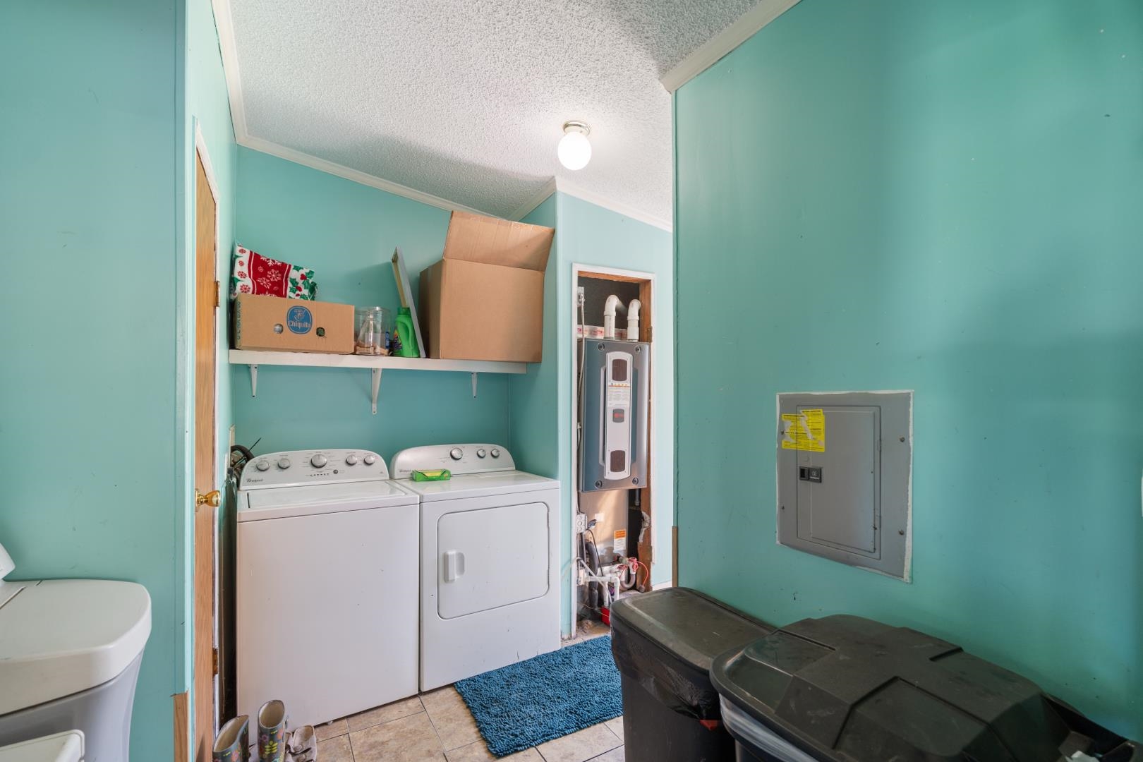 Laundry area with electric panel, ornamental molding, a textured ceiling, separate washer and dryer, and light tile patterned floors